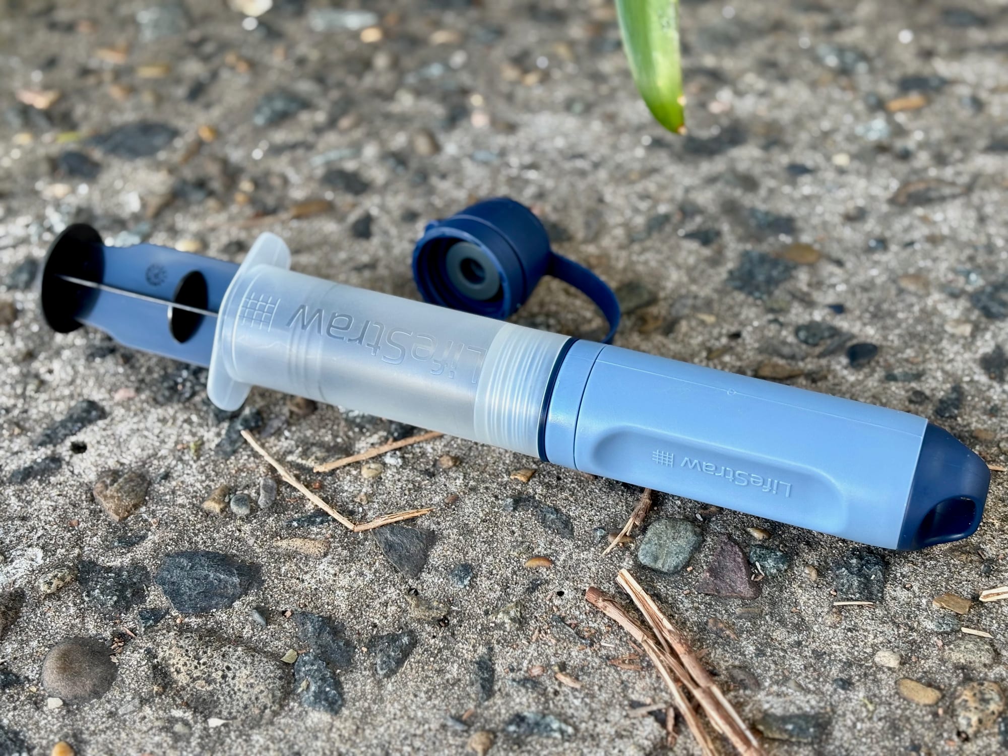 The backwash syringe pushed onto the Peak Solo, with the top cap off beside it, on concrete