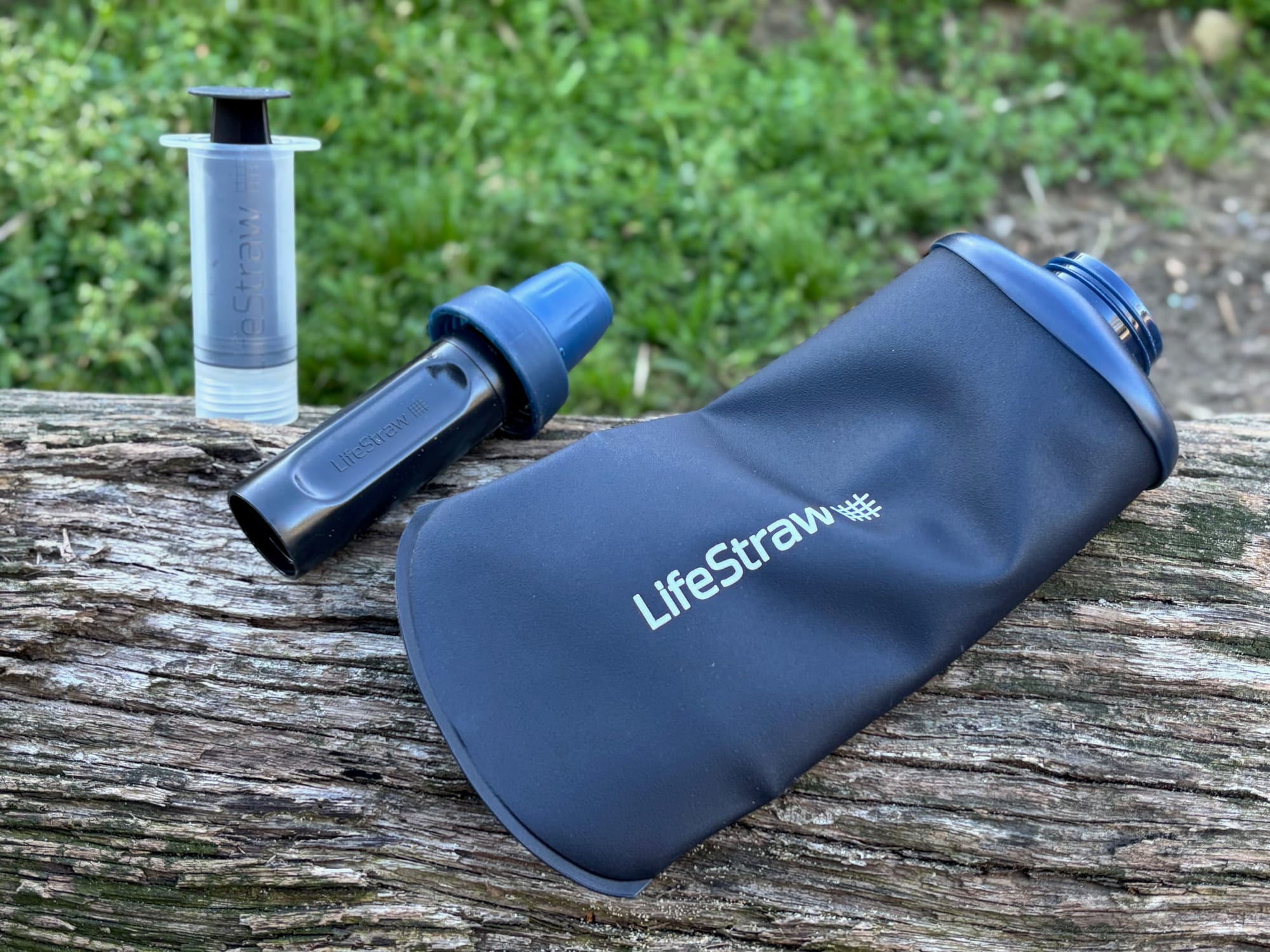 LifeStraw Peak Squeeze collapsible bottle in Mountain Blue on a log, with its filter and syringe