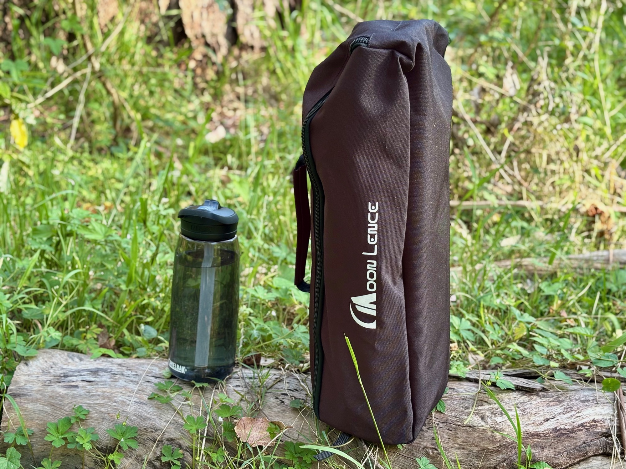 The Moon Lence high back chair packed in its brown bag next to a water bottle