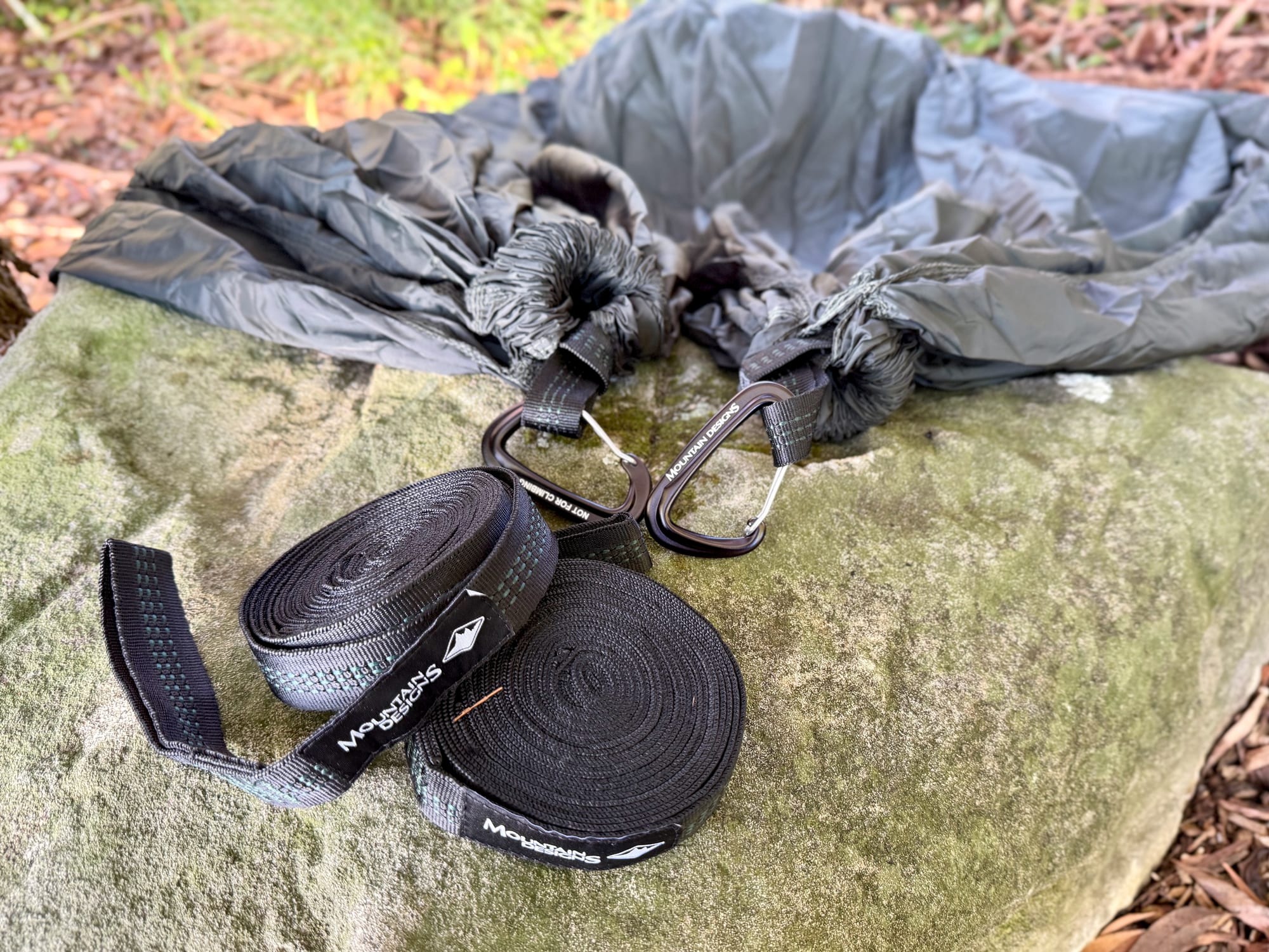 The two black Mountain Designs tree straps and the hammock’s carabiners laid out on a rock