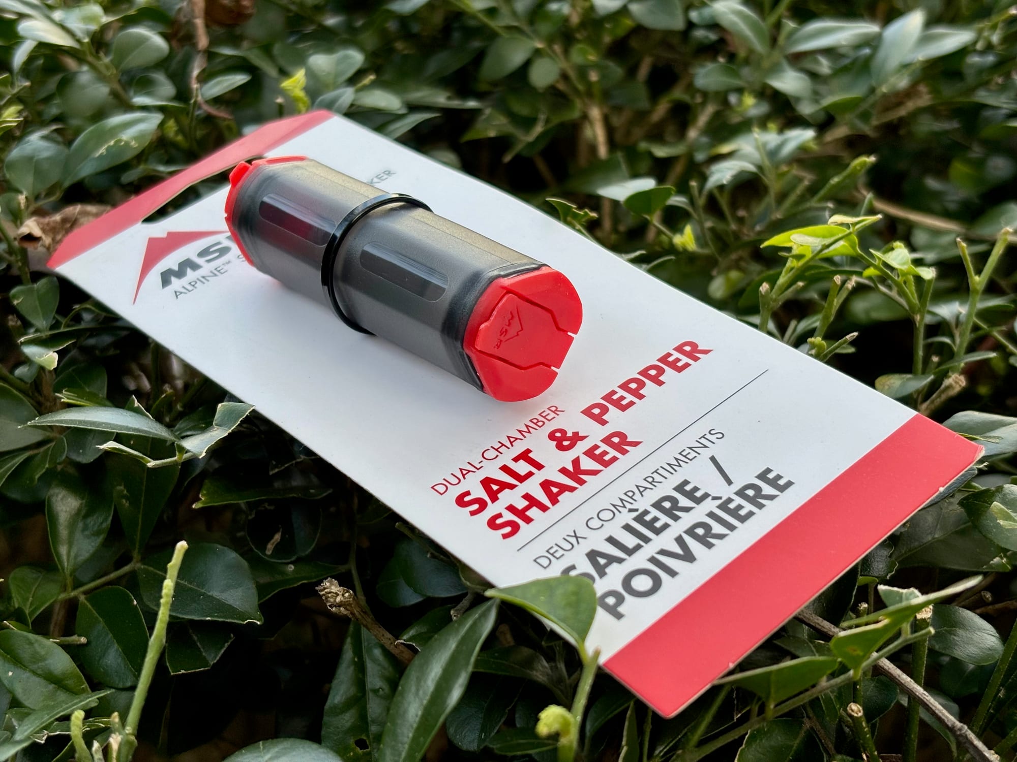 The MSR Alpine salt and pepper shaker in its red and white dual-chamber card pack, lying on a bush