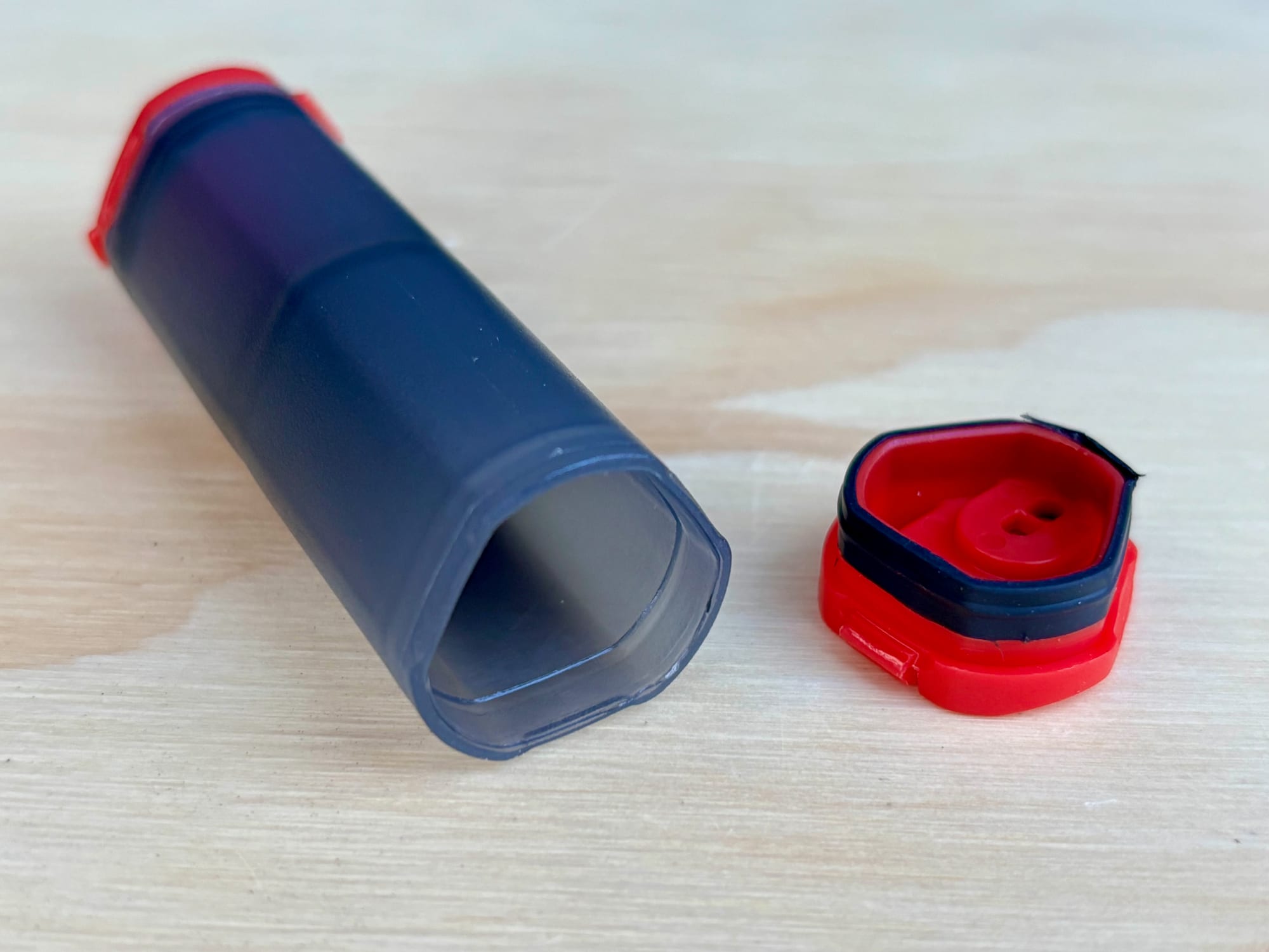 The empty MSR shaker lying on a timber board with one red end cap unscrewed, showing the seal inside the cap