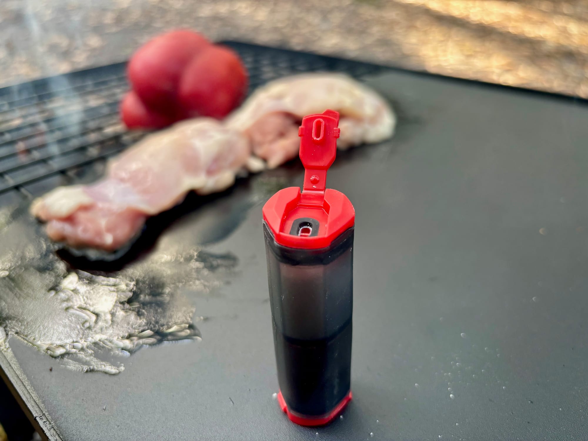The MSR shaker on a camp hotplate with its red flip-top lid open, chicken and a capsicum behind