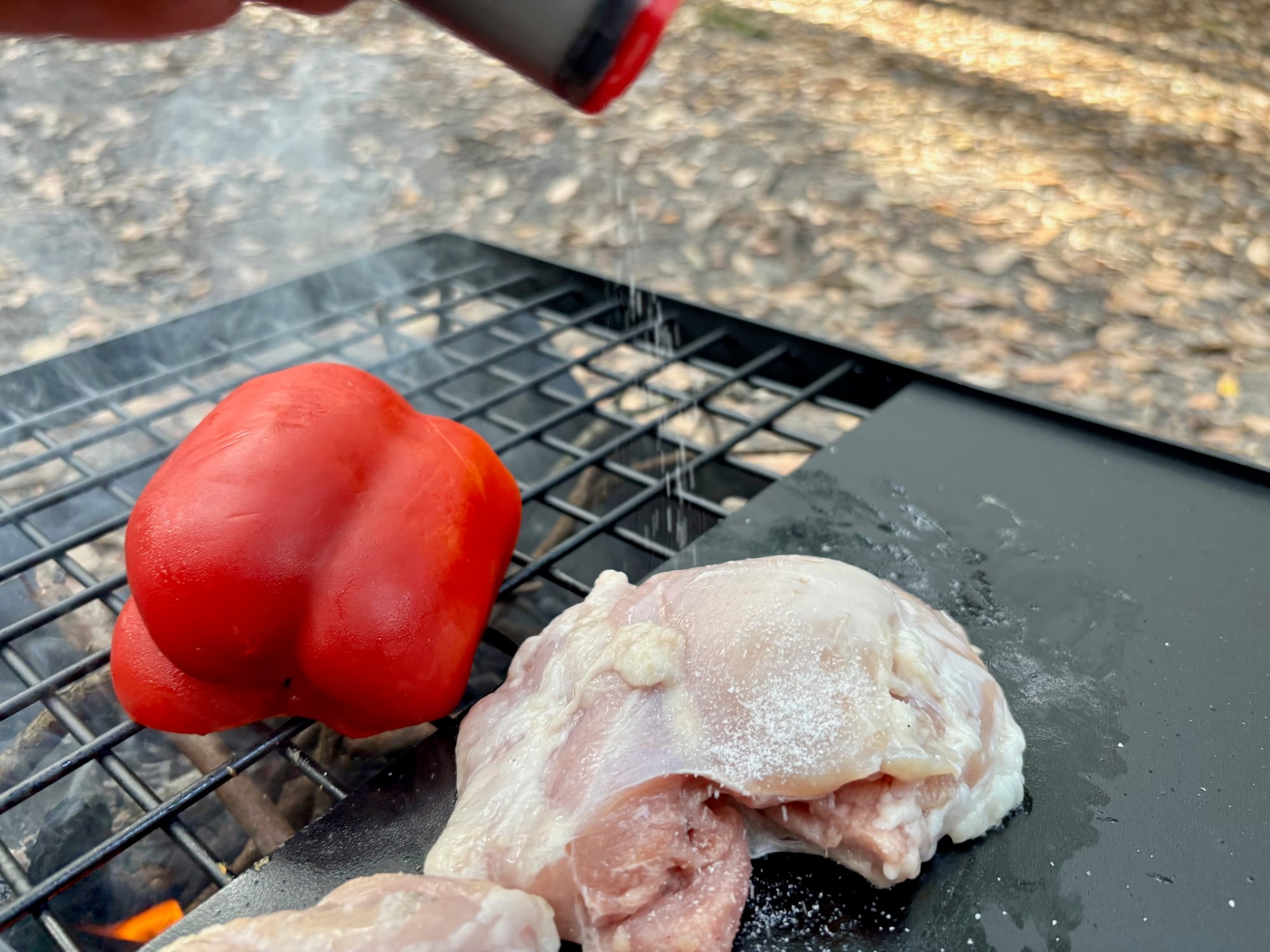 Seasoning chicken on a camp hotplate with the MSR shaker, a red capsicum next to it