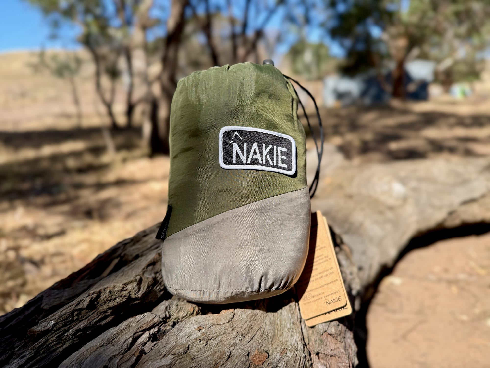 The Nakie hammock packed in its stuff sack on a log, with the hang tag