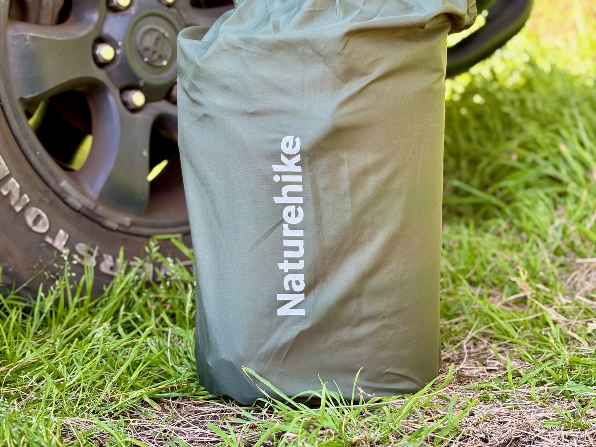 The Naturehike D-Series sleeping pad in its carry bag, standing next to a 4WD wheel