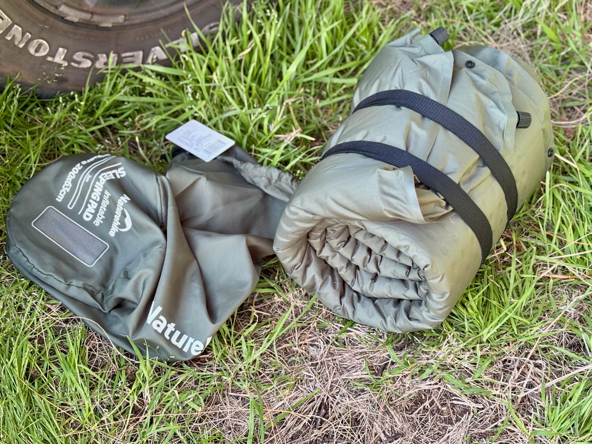 The Naturehike D-Series sleeping pad rolled up with two straps, next to its carry bag