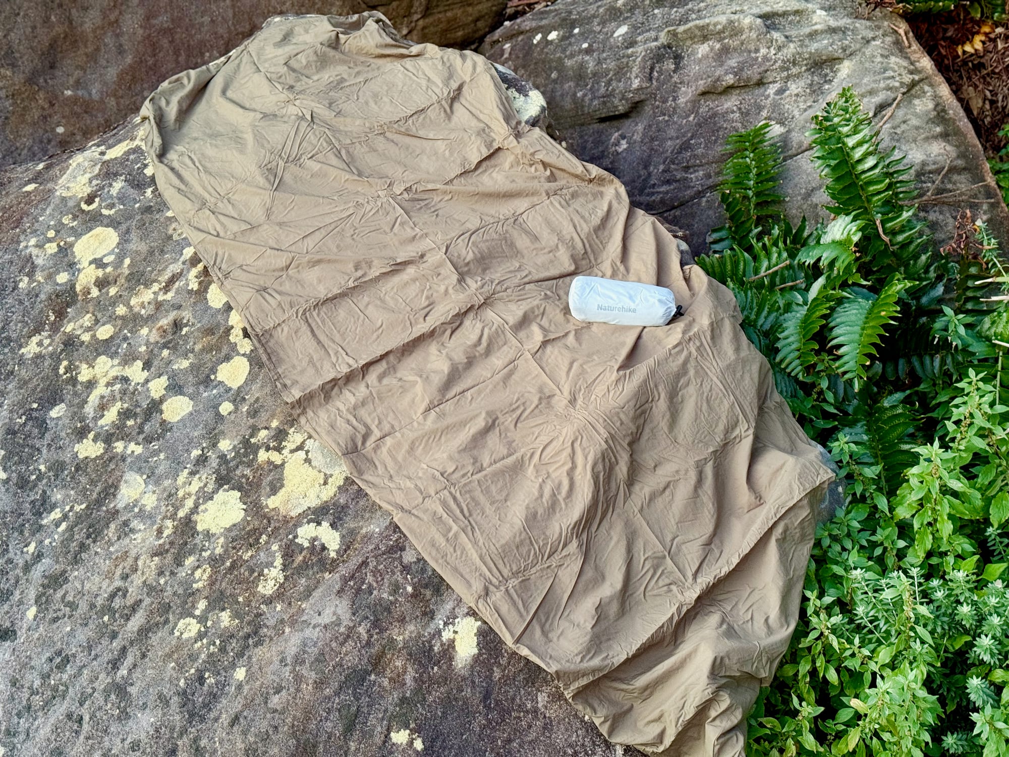 The Naturehike sleeping bag liner laid out at full length on a rock, with its stuff sack on top
