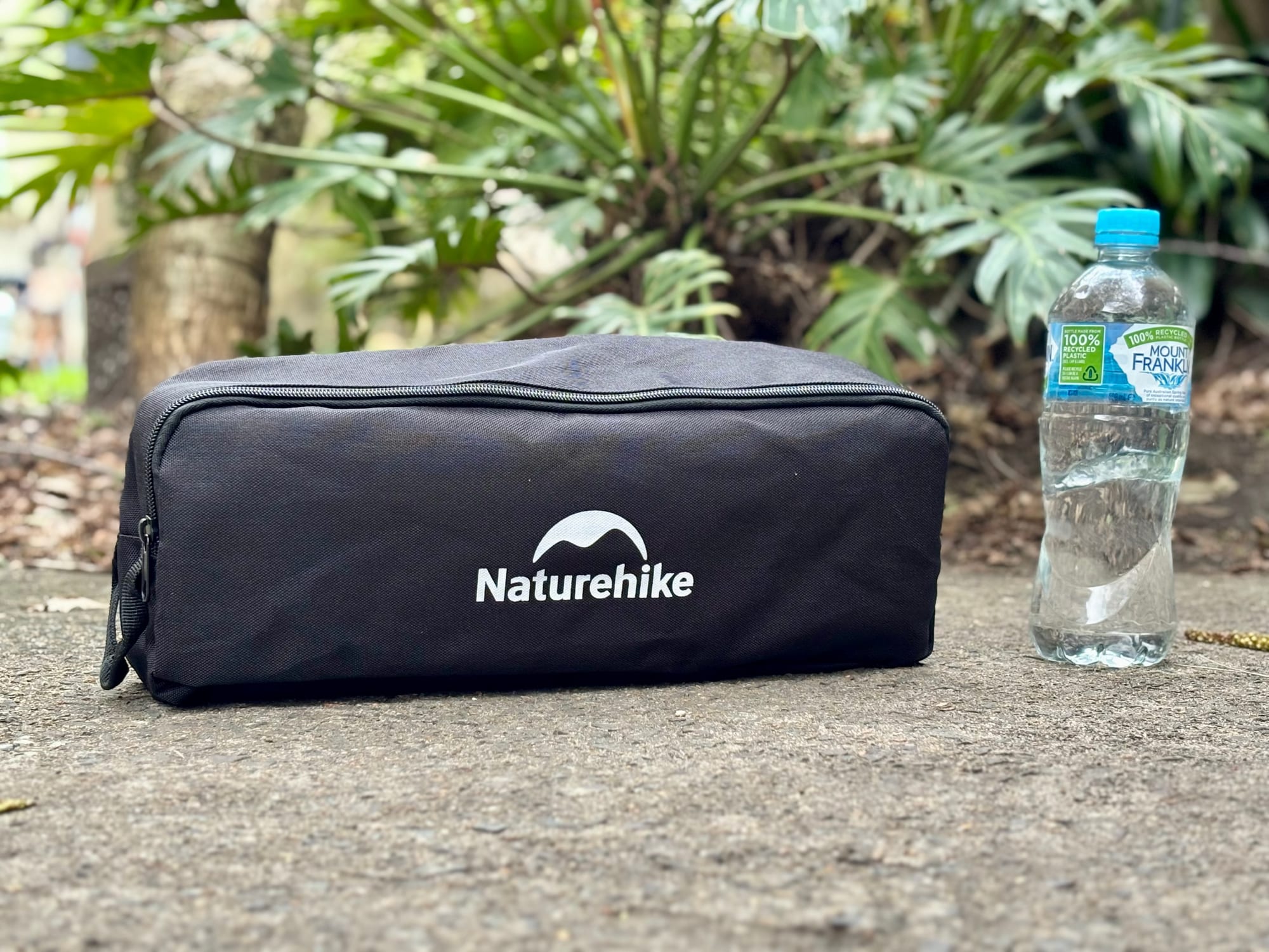 The Naturehike YL01 packed in its black carry bag next to a water bottle