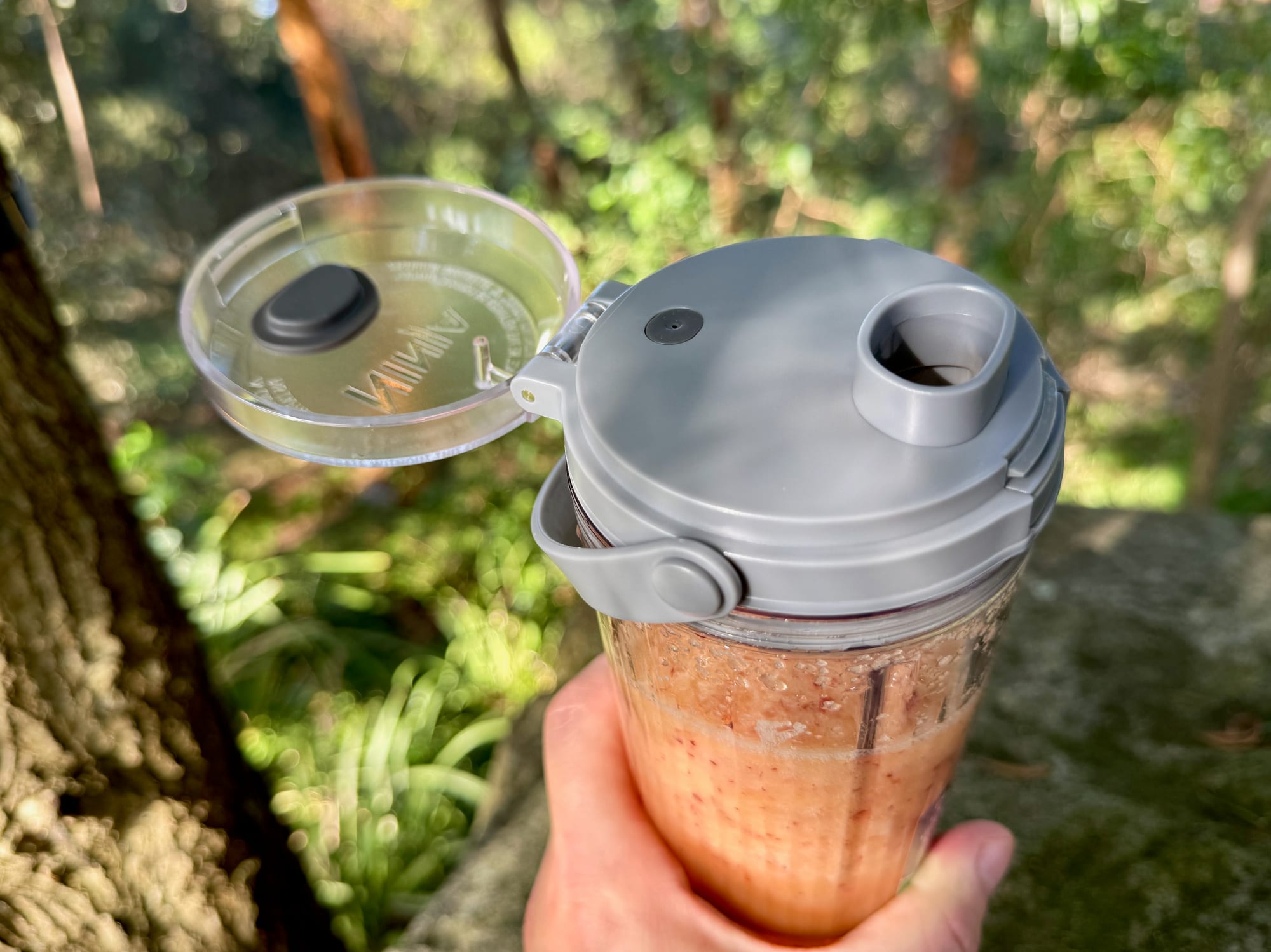 A hand holding the Ninja Blast with the sip lid flipped open and a smoothie inside