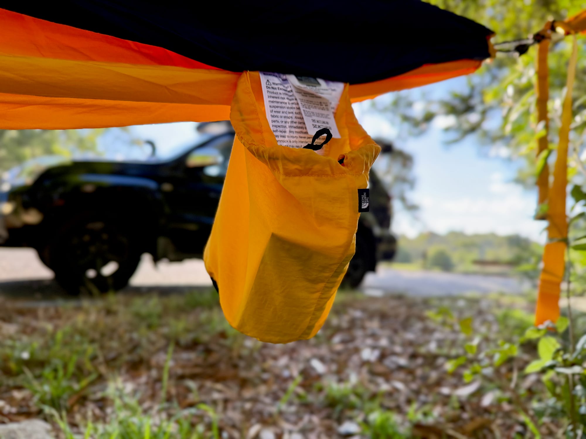 The empty gold stuff sack hanging from the side of the hammock as a pocket, with a 4WD behind
