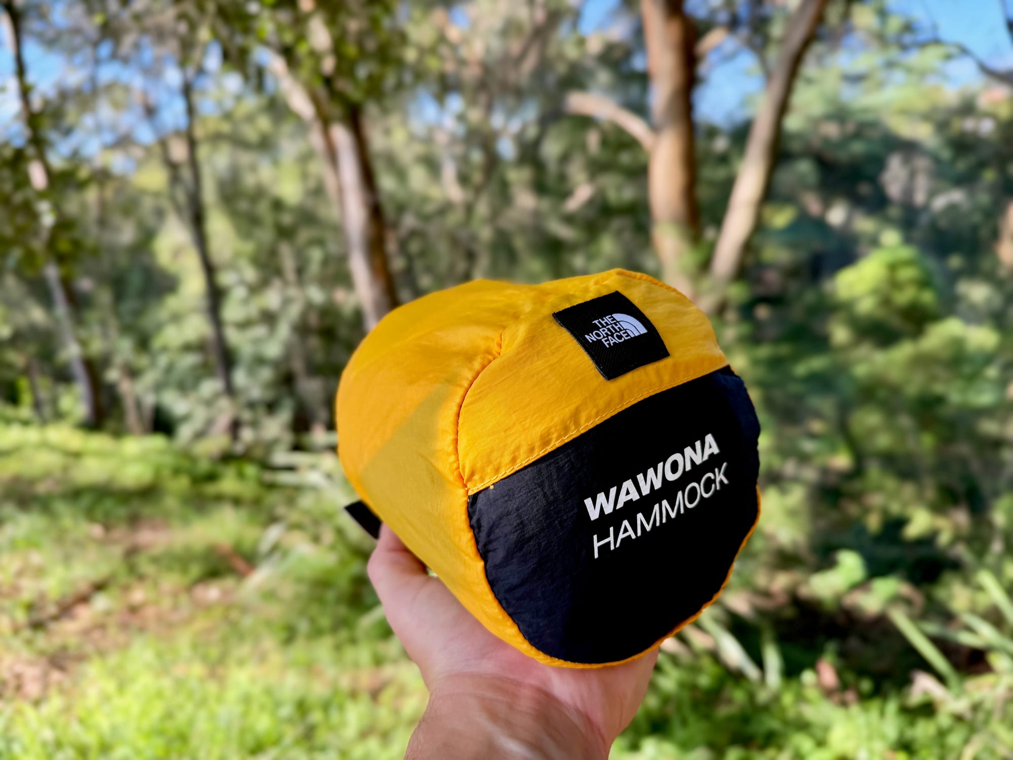 The packed North Face Wawona hammock in its gold stuff sack, held in one hand in the bush