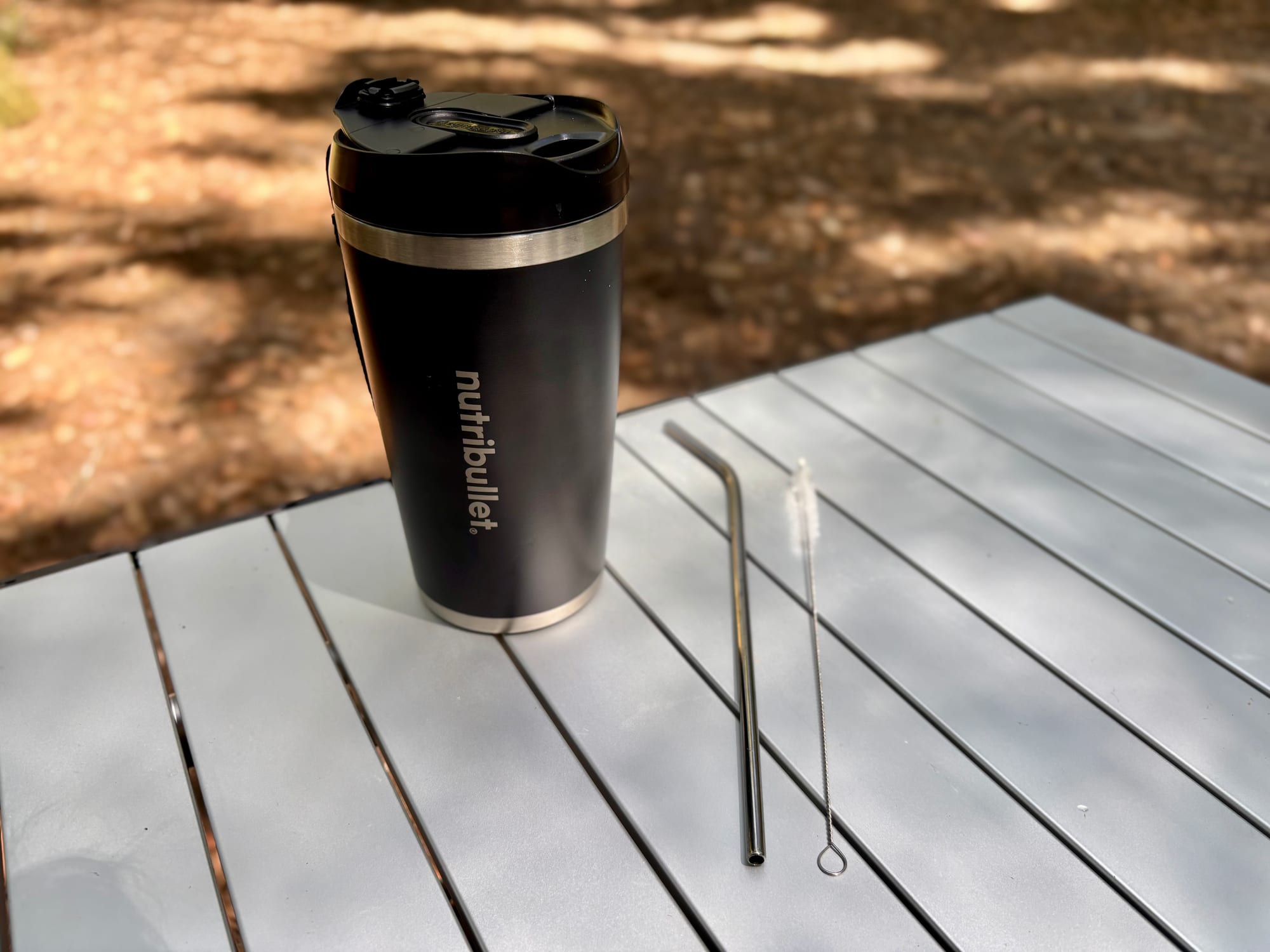 The NutriBullet Flip with its to-go lid on, next to the straw and cleaning brush