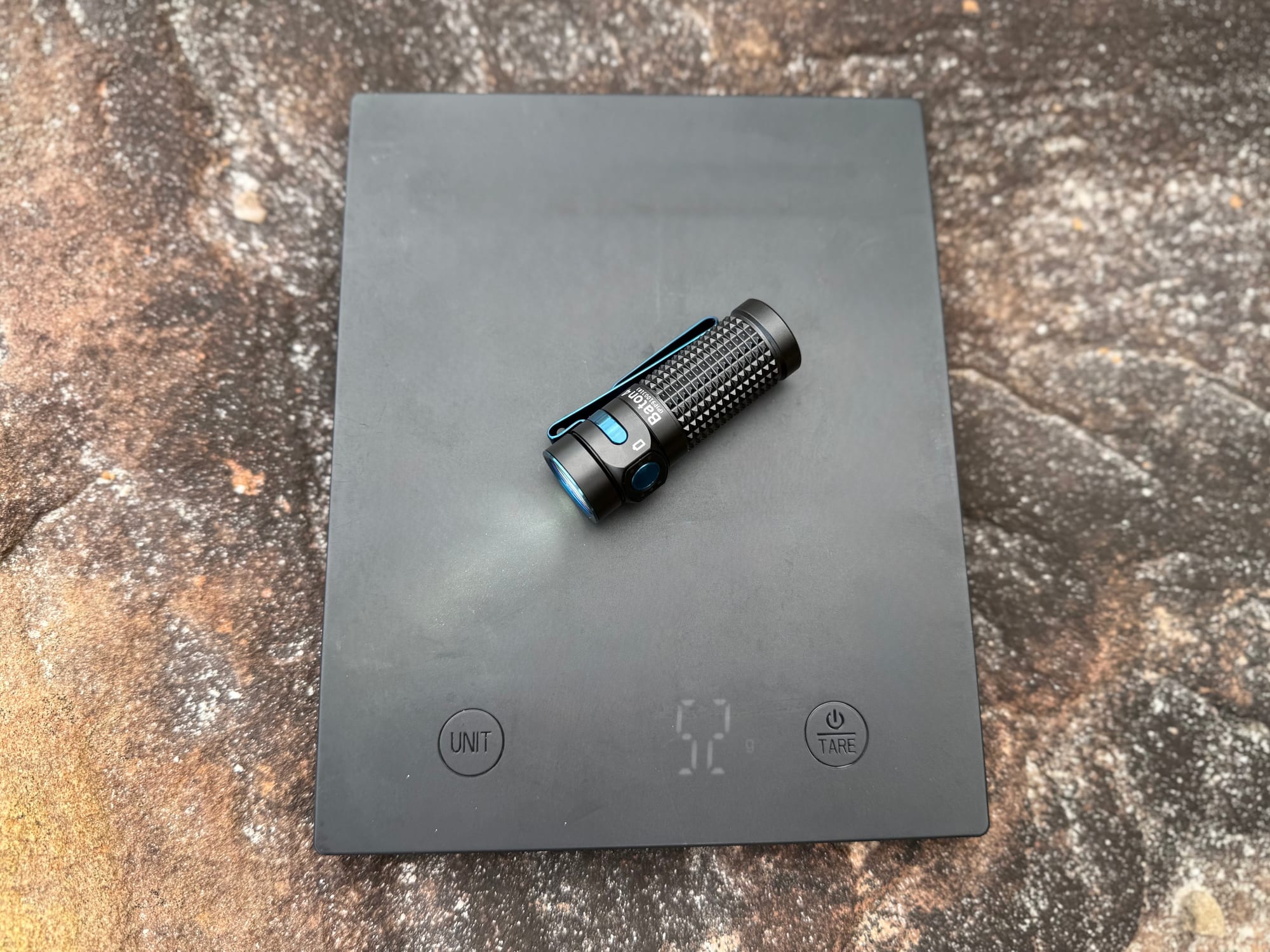 The Olight Baton 4 switched on, lying on a kitchen scale showing 52 g