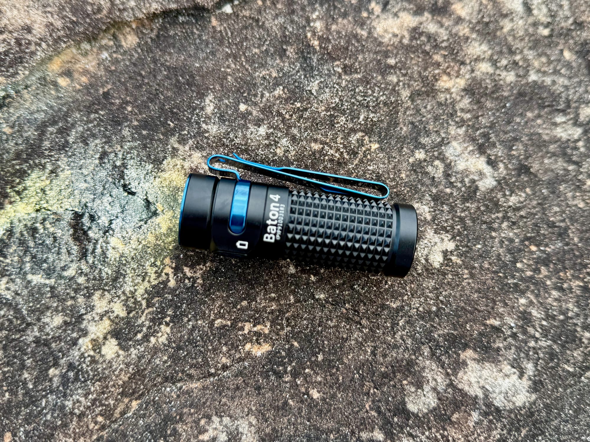 The Baton 4 on a rock, showing the blue side switch and the pocket clip