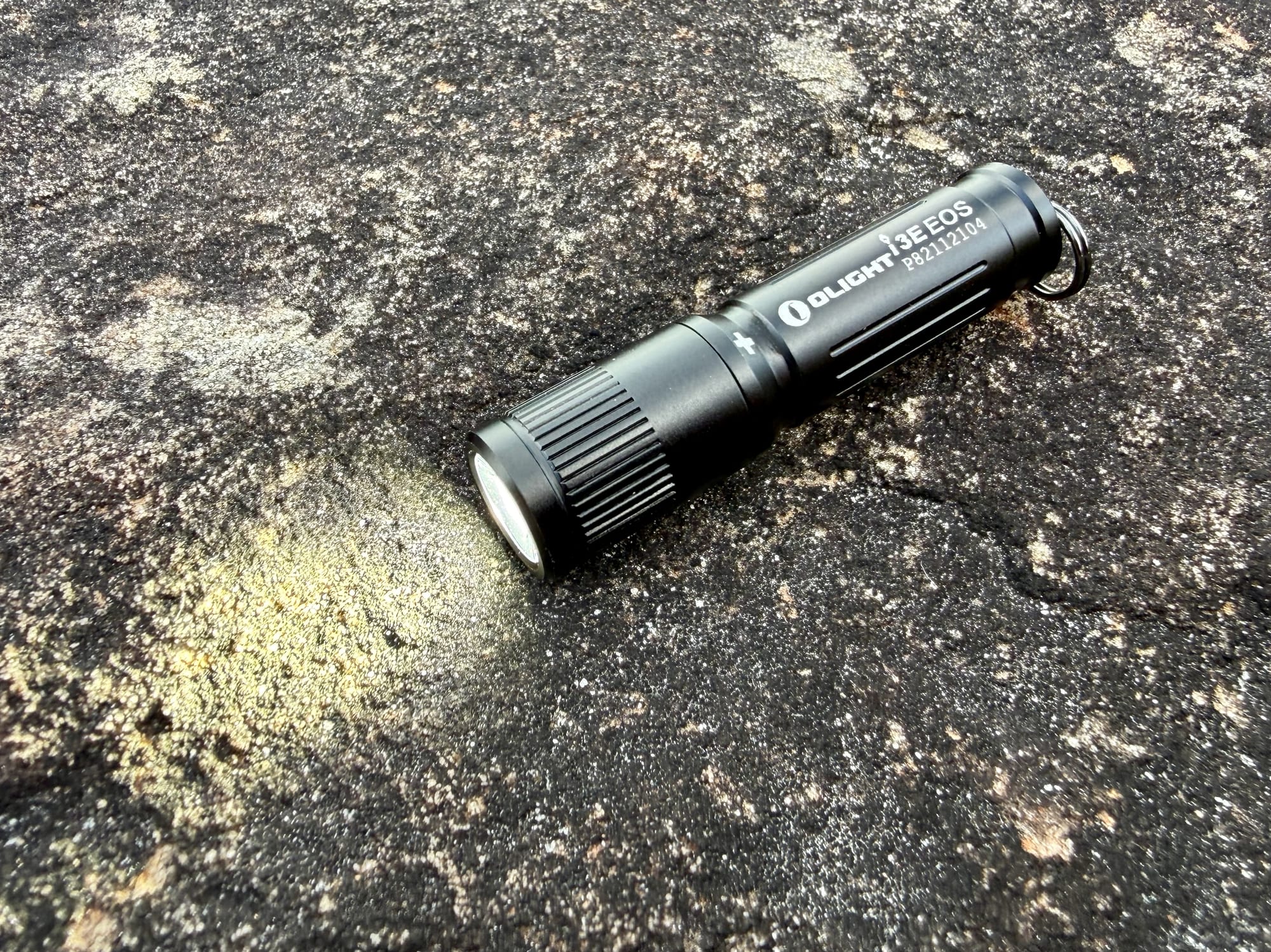 The Olight i3E EOS switched on, lighting up the rock in front of it