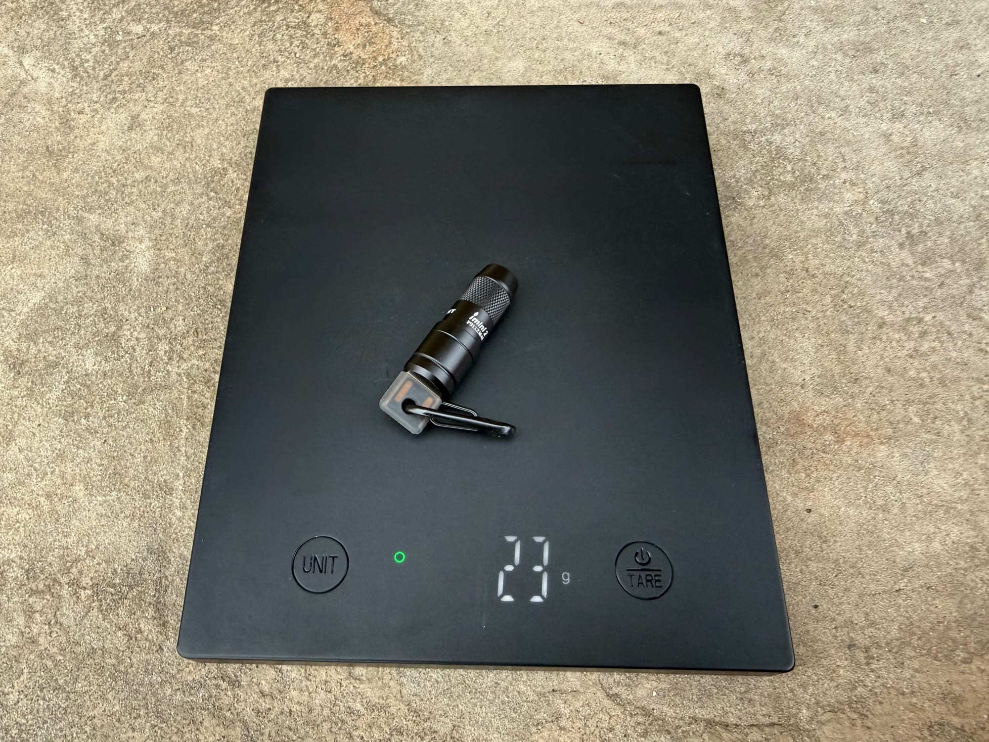 The Olight iMini 2 on a digital scale showing 23 grams with its carabiner