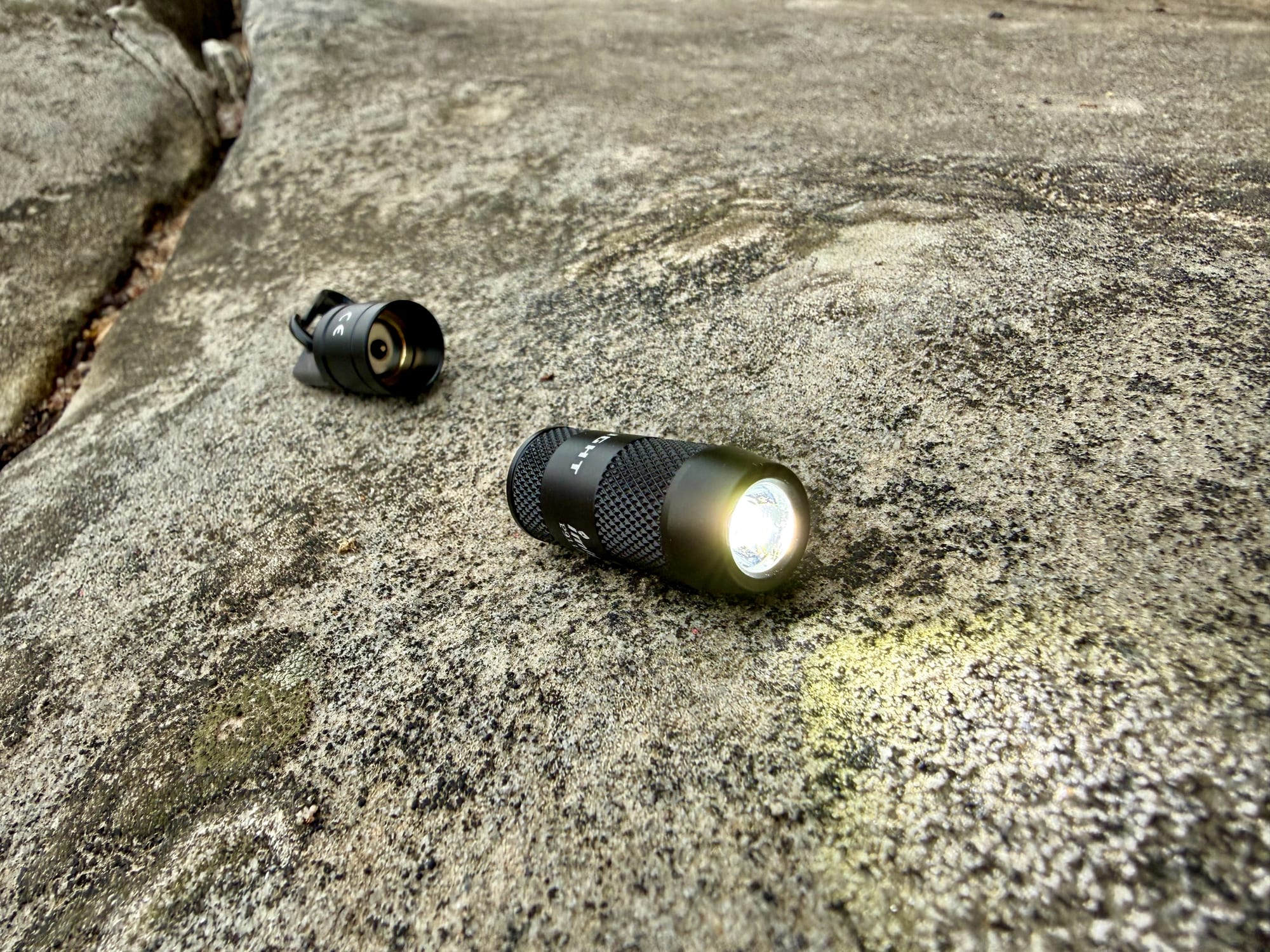 The Olight iMini 2 switched on, pulled off its cap, on a rock