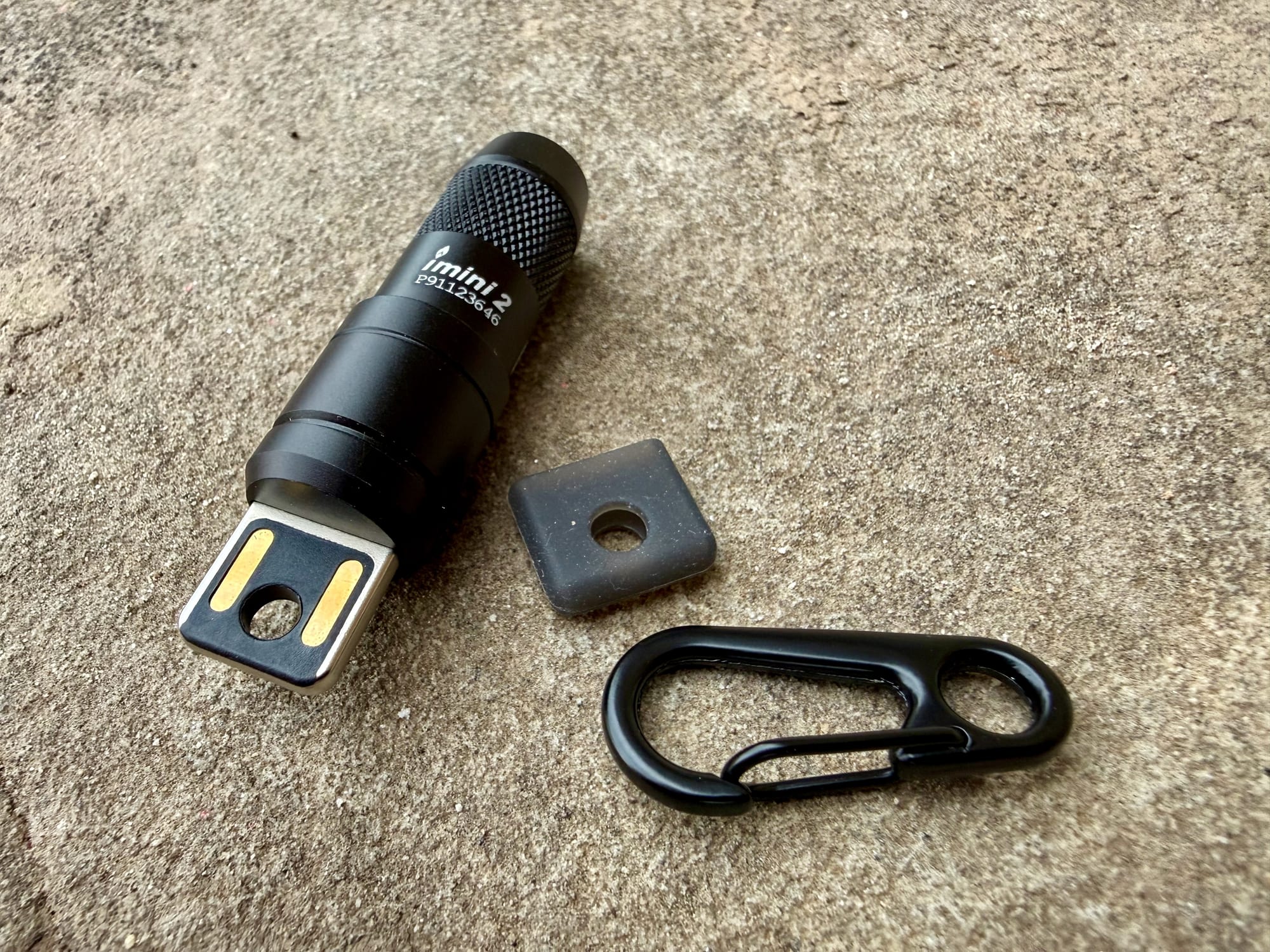 The Olight iMini 2 with its USB plug on the end, the square plate and the carabiner