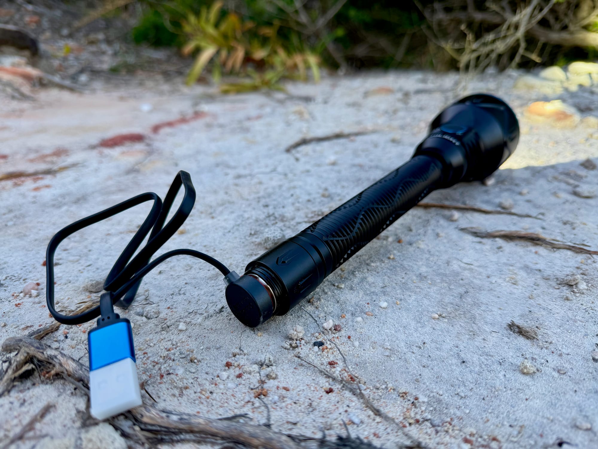 The Javelot Pro 2 on a rock with the Olight MCC3 magnetic USB cable clipped onto its tail