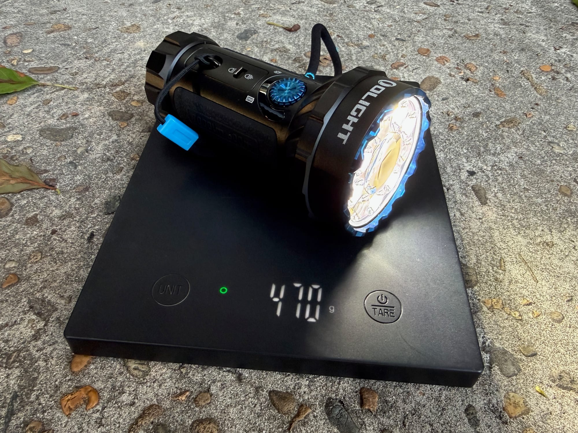 The Olight Marauder Mini switched on, on a kitchen scale showing 470 g