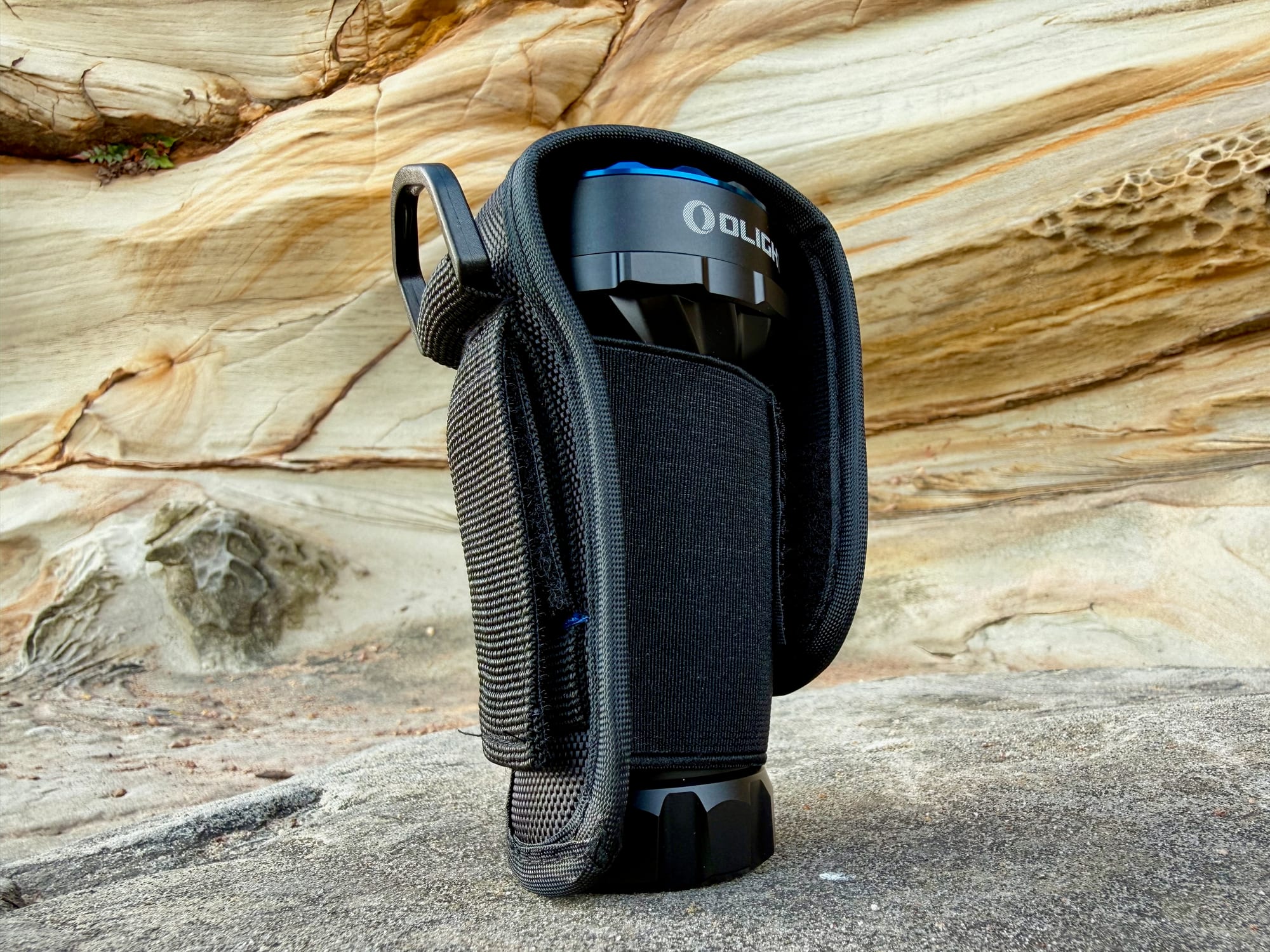The Olight Marauder Mini standing in its nylon holster on a rock