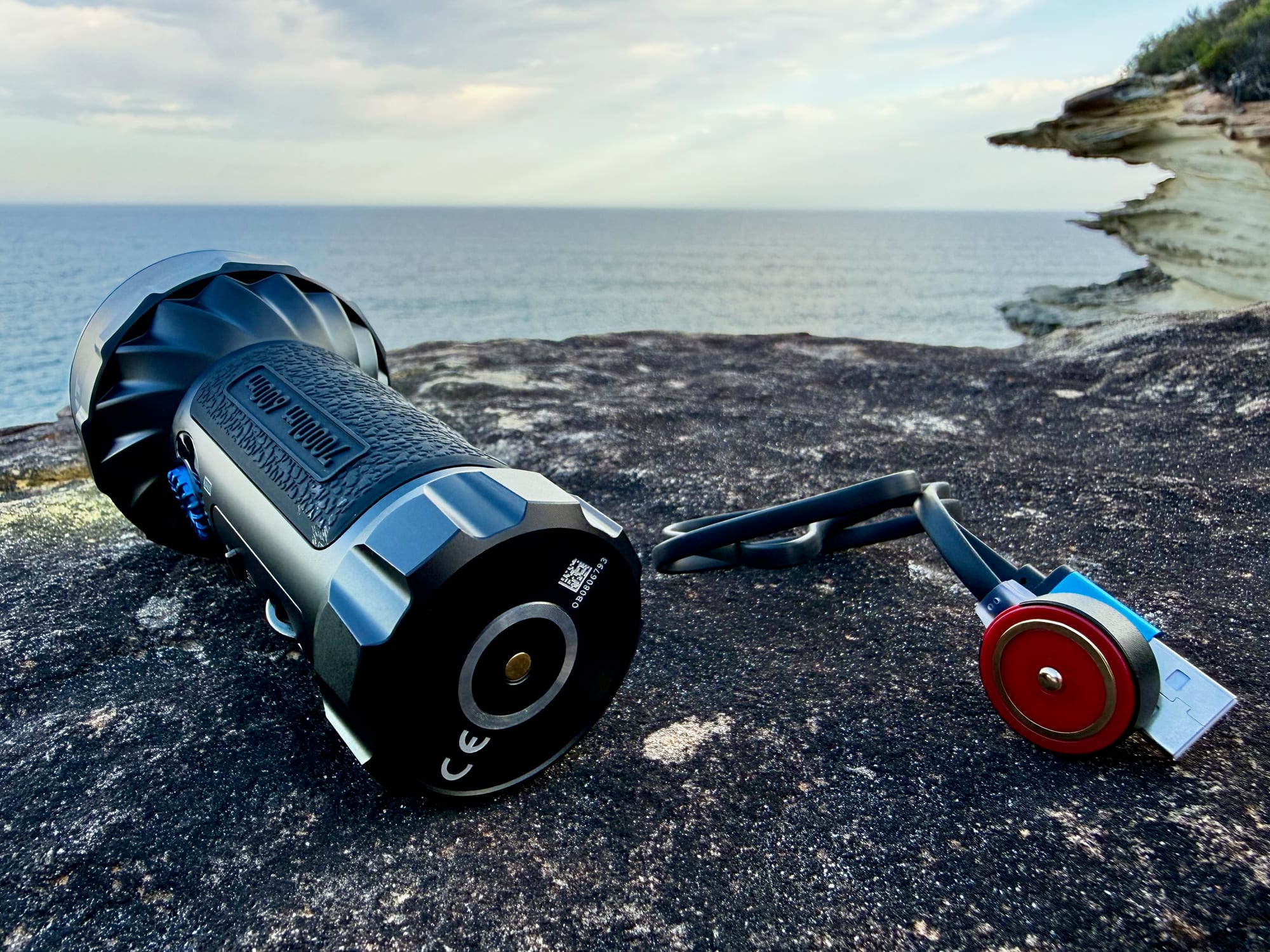 The tail of the Olight Marauder Mini with its round magnetic contact, next to the red magnetic charging cable