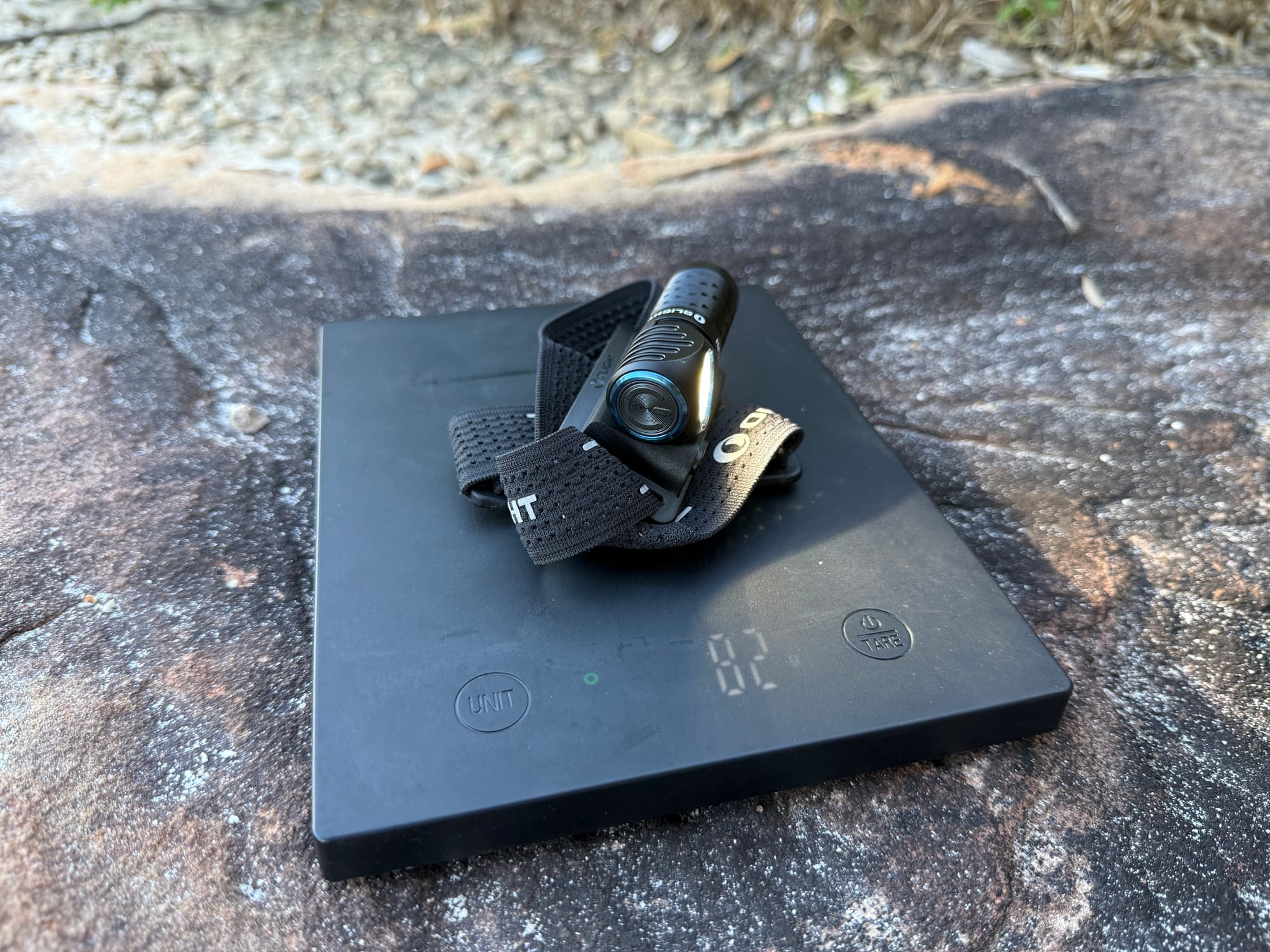 The Olight Perun 3 Mini in its headband on a kitchen scale showing 82 g