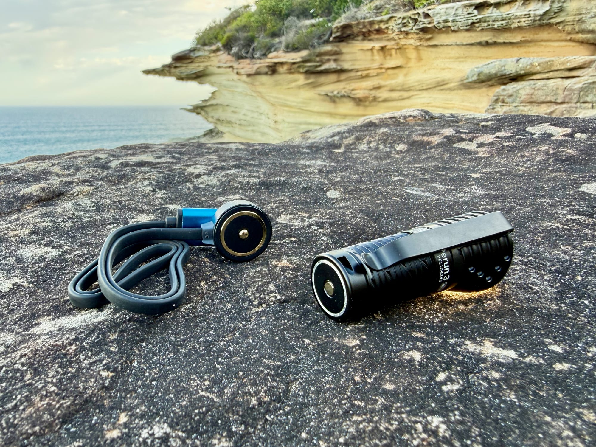 The Olight Perun 3 Mini next to its magnetic charging cable, on a rock