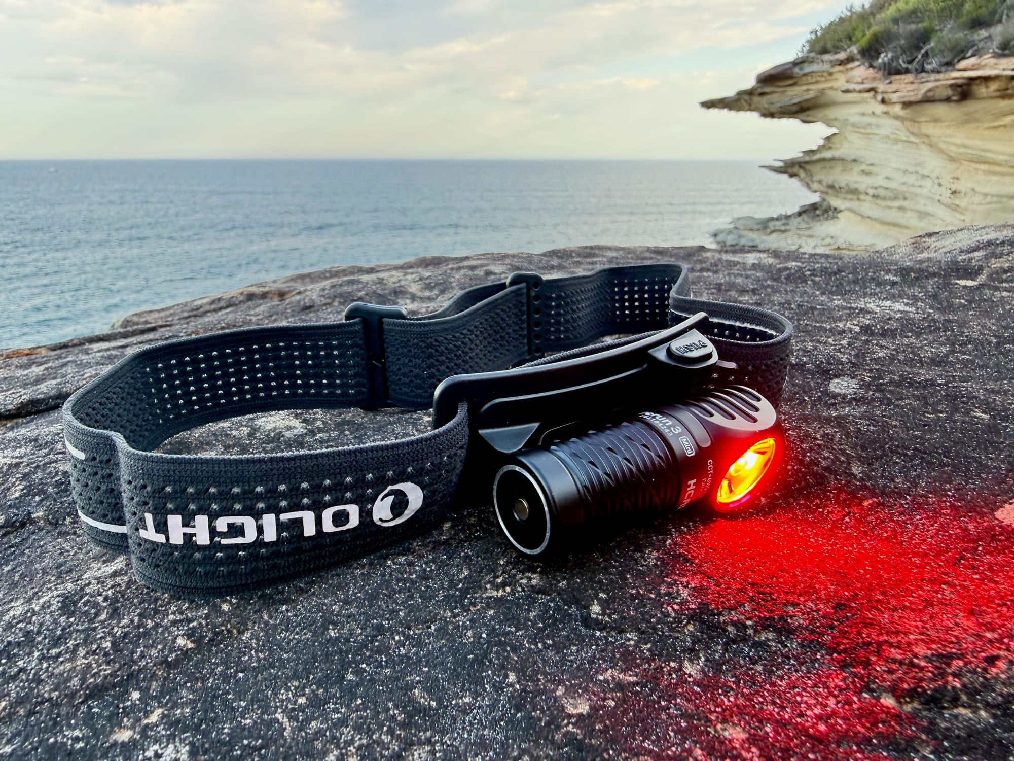 The Olight Perun 3 Mini in its headband with the red light on, lighting up the rock in front of it