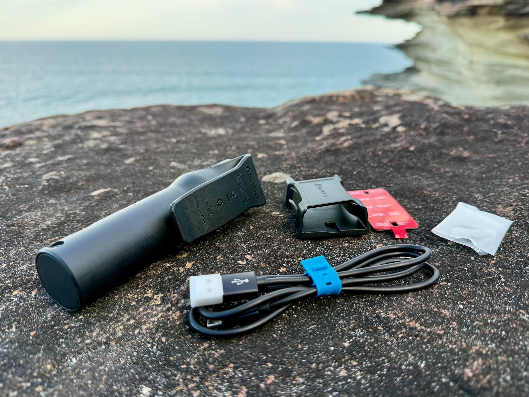 The Olight Seeker 4 Pro with its holster and USB-C cable laid out on a rock