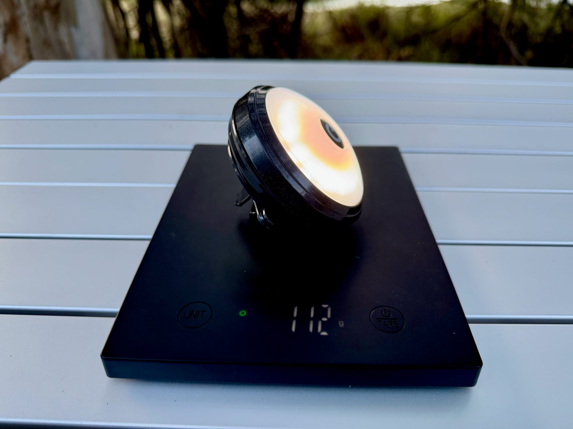 The OZtrail Portable Camp Light on a scale showing 112 g