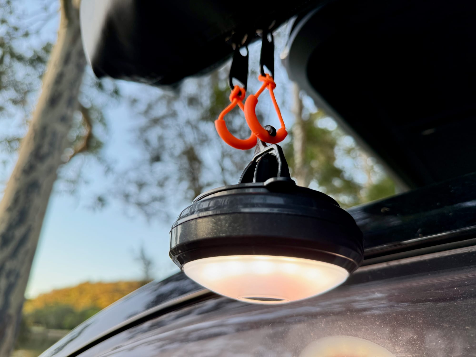 The OZtrail Portable Camp Light on white, hanging from carabiners under the rooftop tent