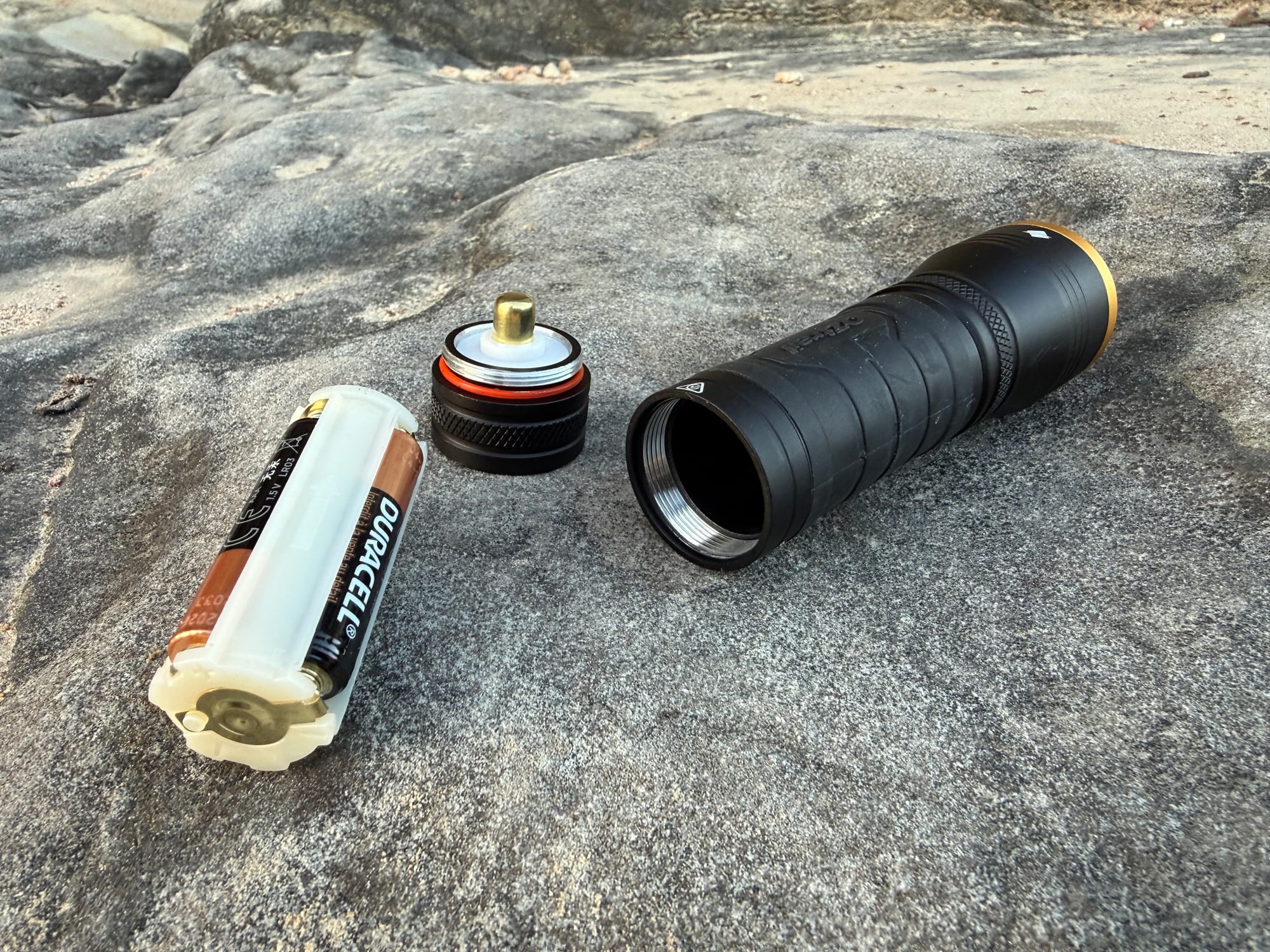 The F300’s tail cap and AAA battery holder taken out of the torch, on a sandstone rock