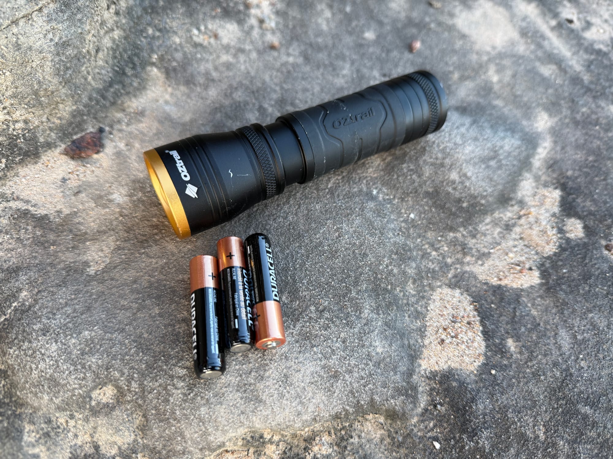 The OZtrail Lumos F300 on a sandstone rock with its three AAA batteries next to it