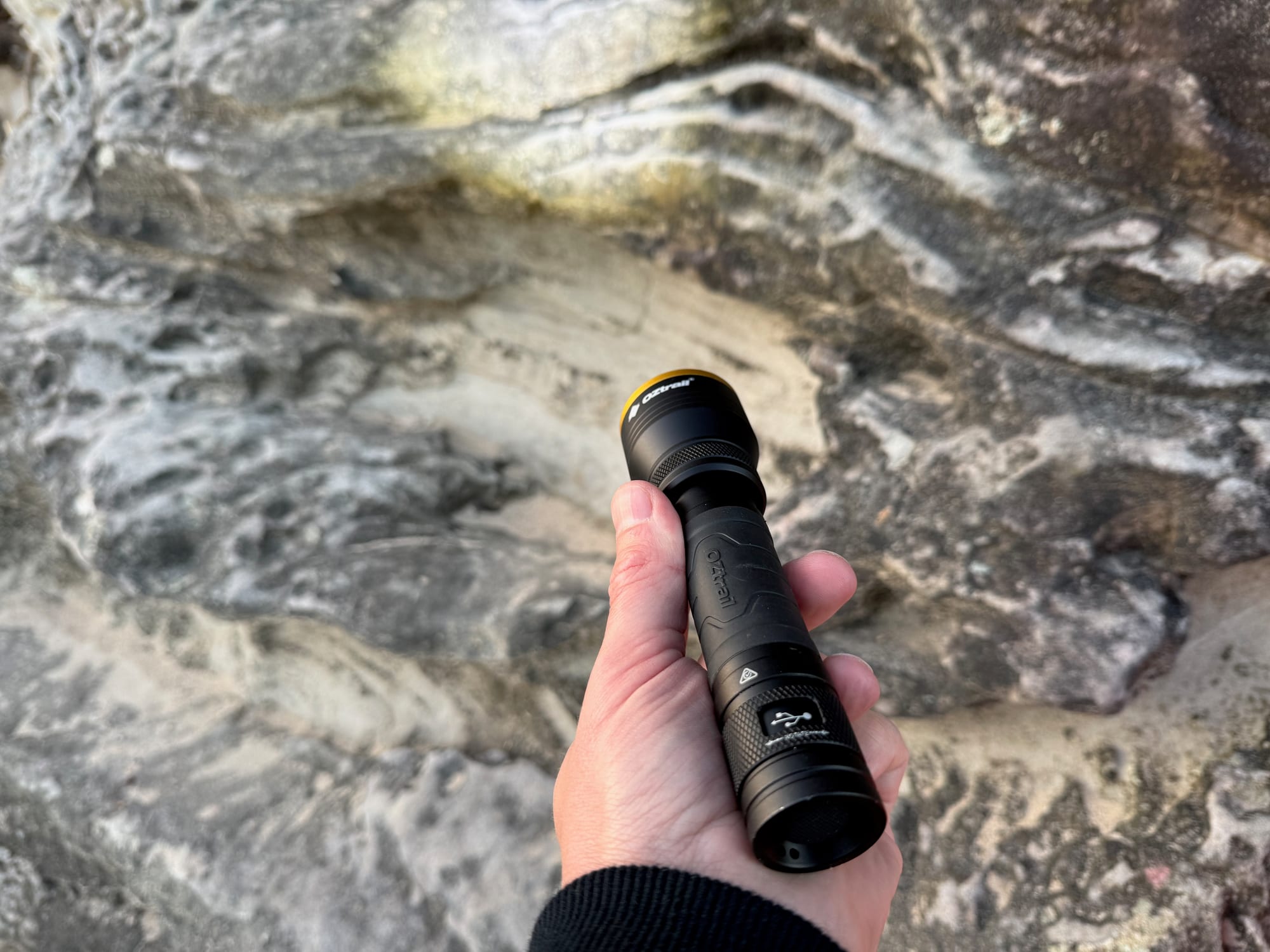 The OZtrail Lumos FR800 held in a hand, its beam lighting up the sandstone ahead