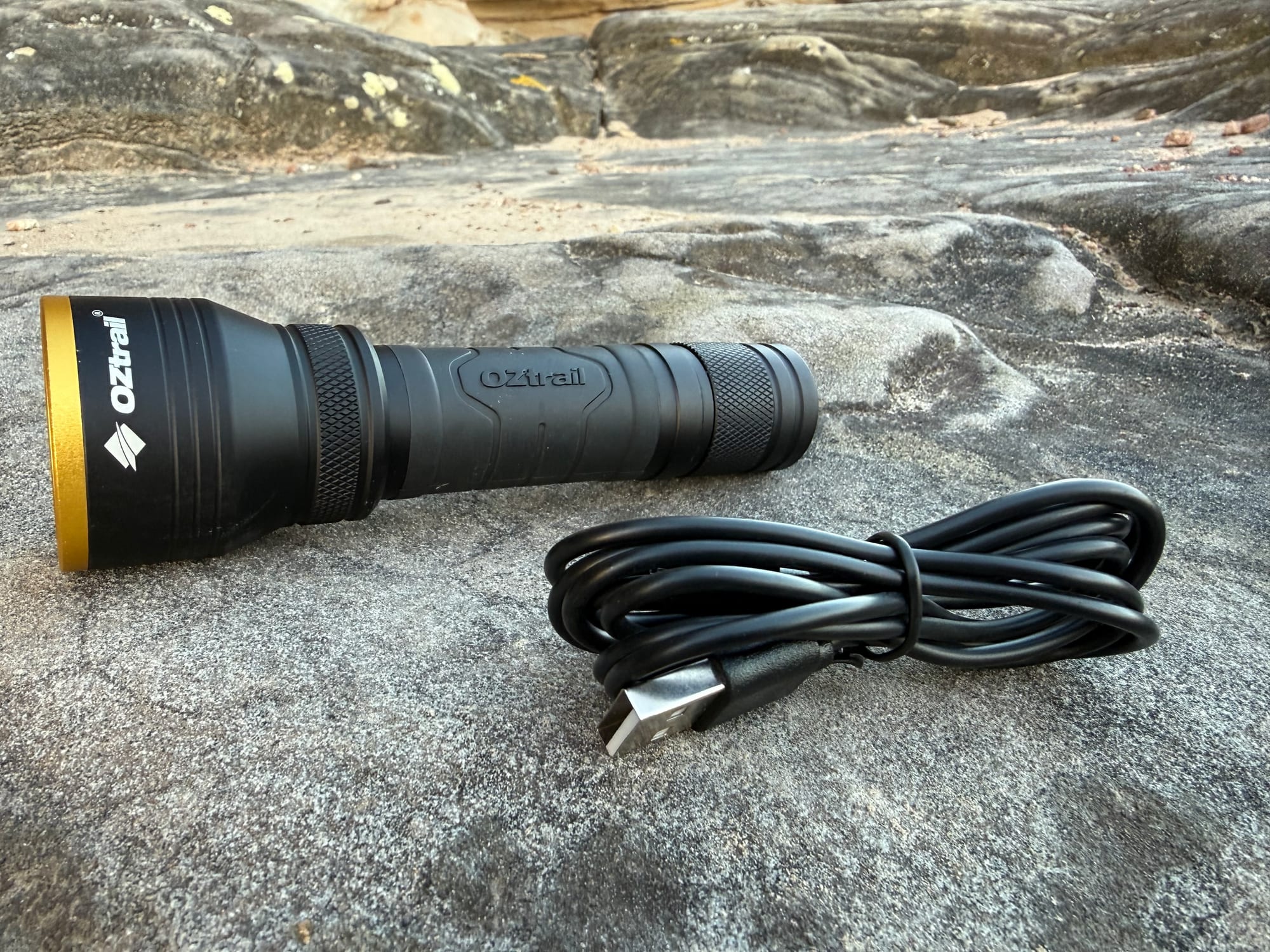 The OZtrail Lumos FR800 lying on a sandstone rock next to its coiled USB-C charging cable