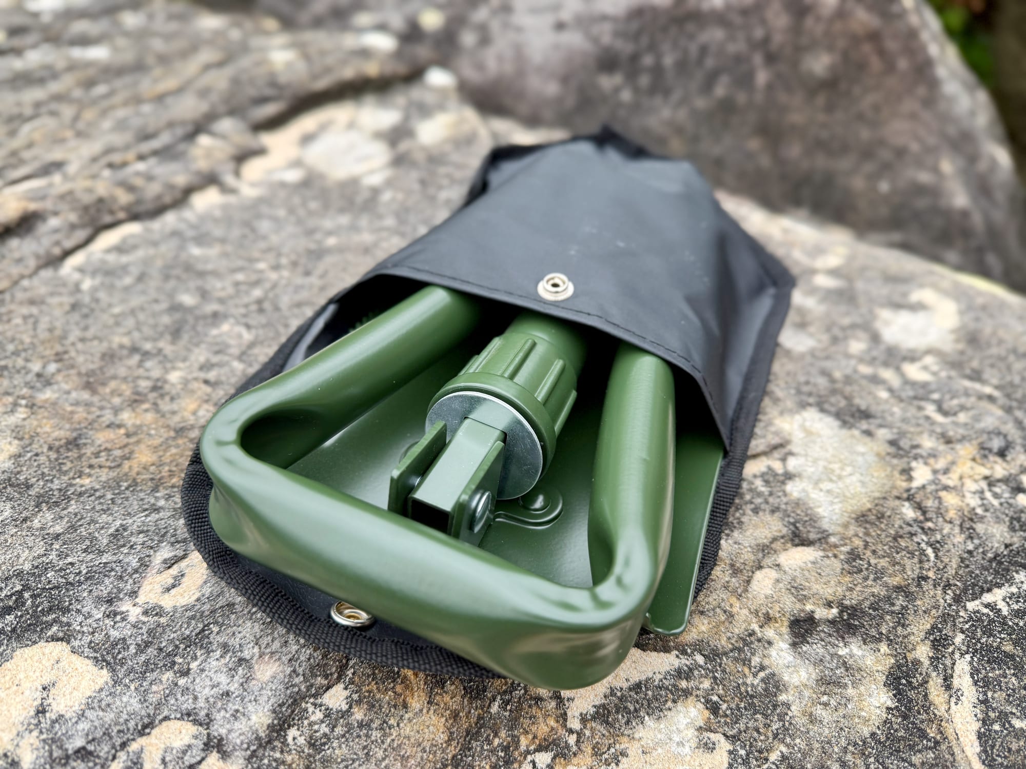 The OZtrail Tri-Fold Shovel folded in three, half inside its black storage bag