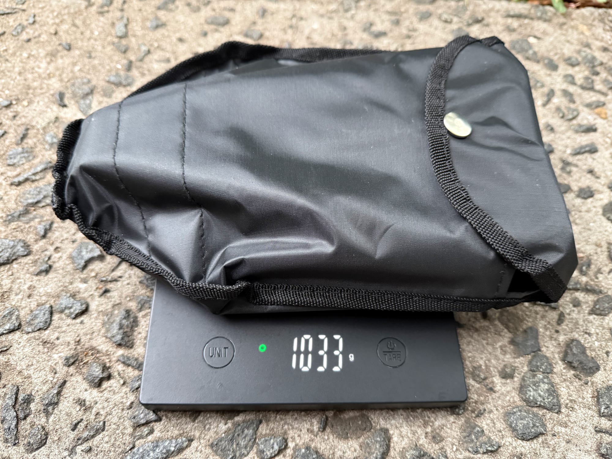 The OZtrail Tri-Fold Shovel in its storage bag on a scale showing 1,033 g