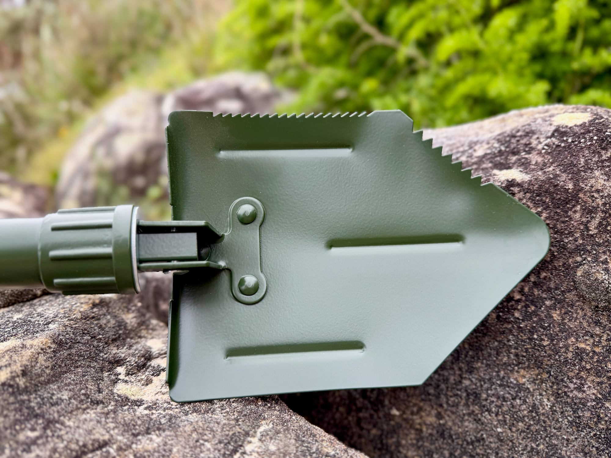 The pointed green blade of the OZtrail Tri-Fold Shovel with its serrated edge, and the locking collar on the shaft