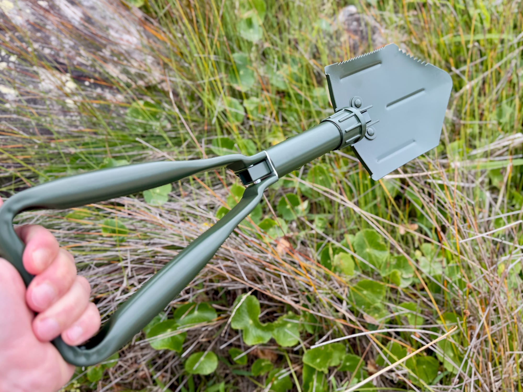 A hand gripping the triangle handle of the unfolded OZtrail Tri-Fold Shovel