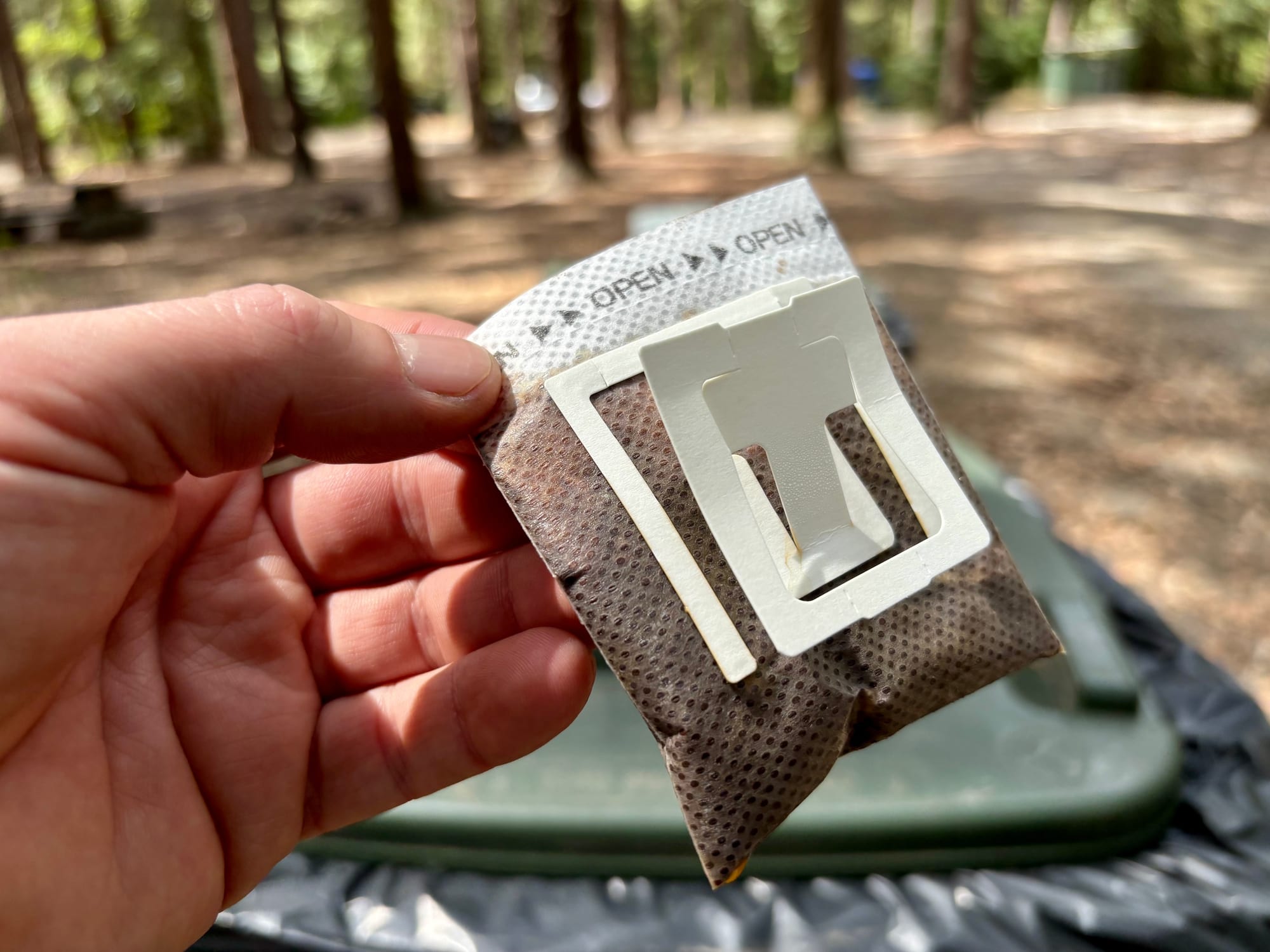 A used drip coffee filter bag held over a rubbish bin