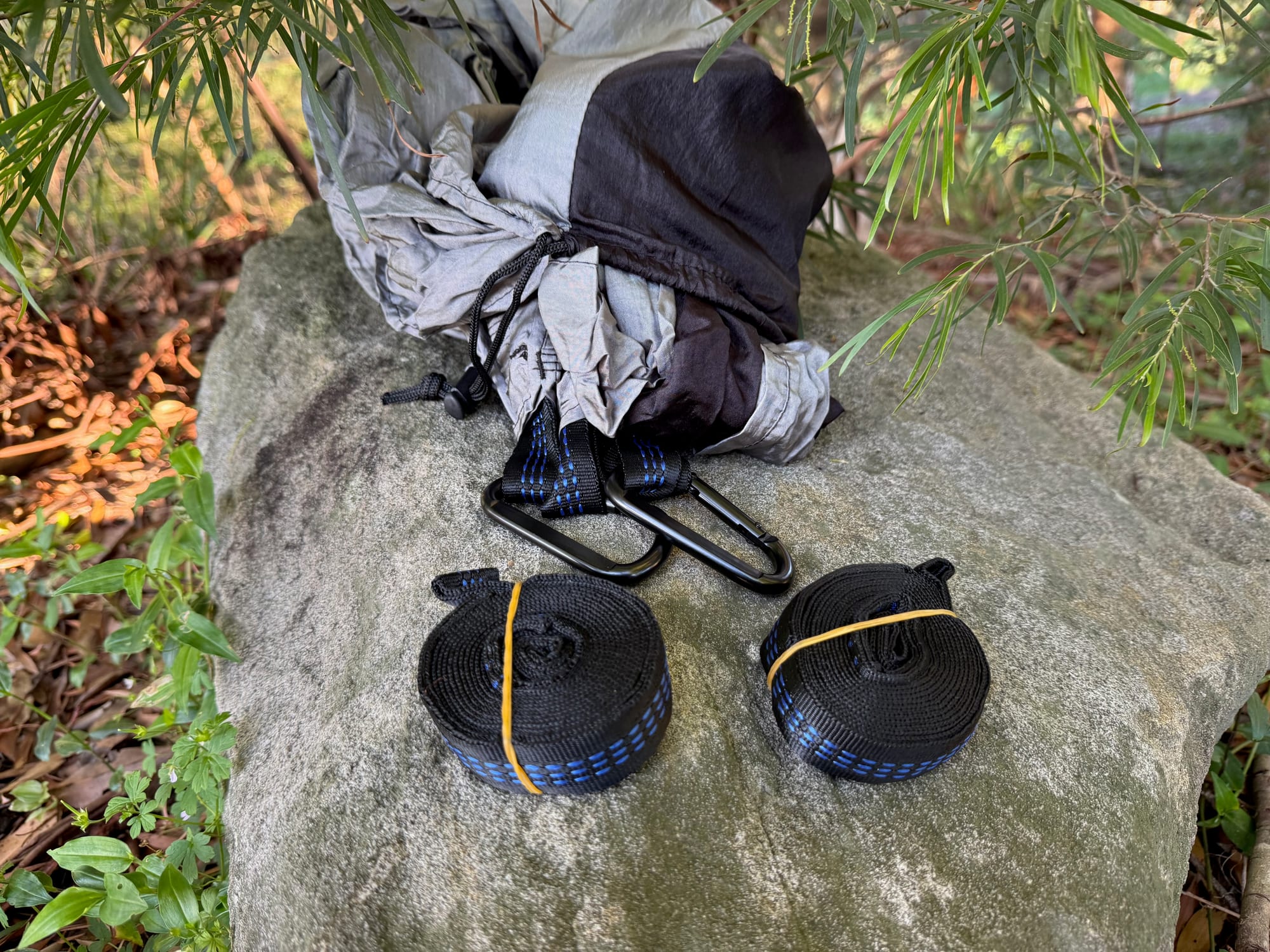 The two blue-and-black tree straps and the black carabiners laid out on a rock