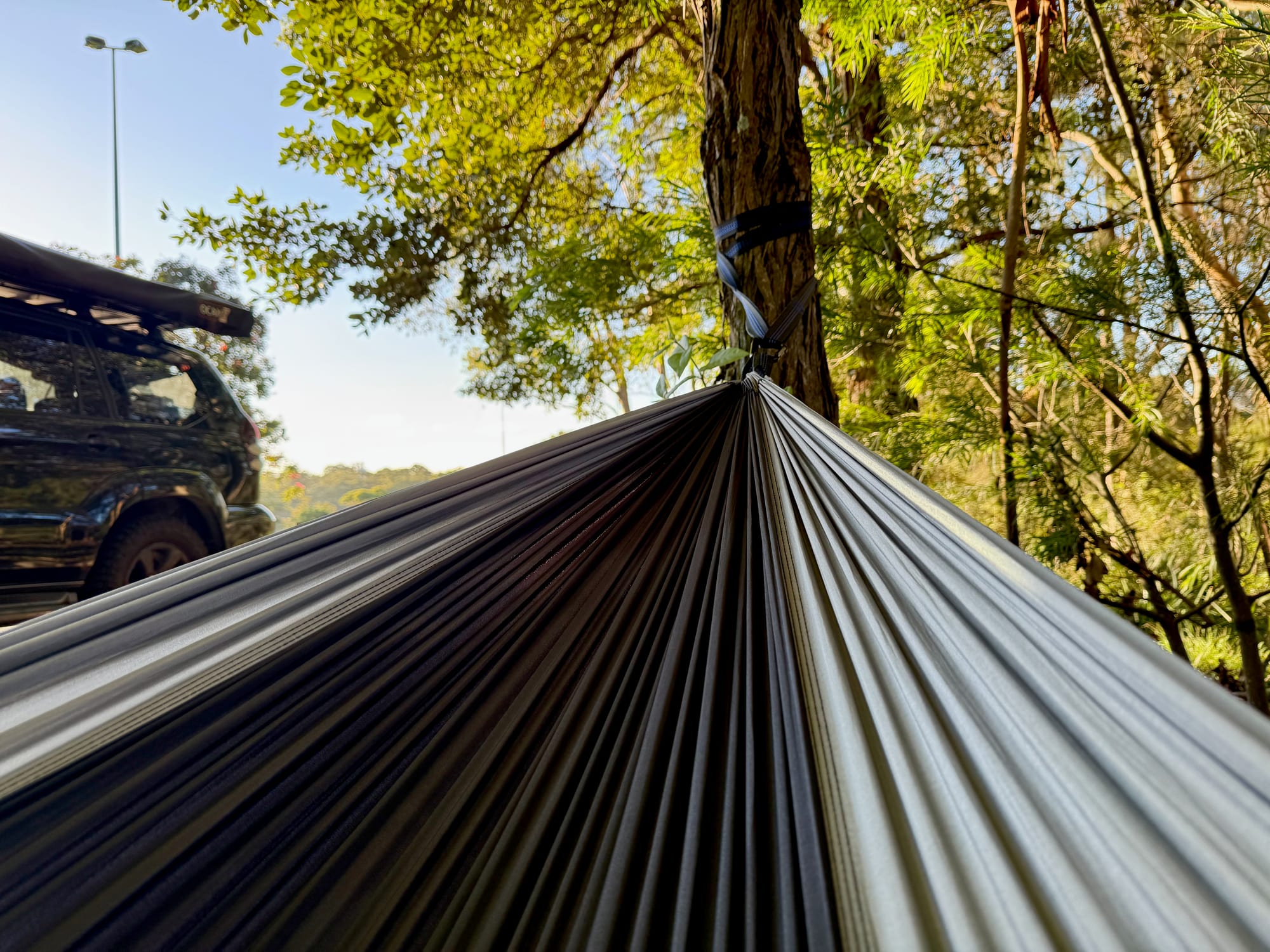 Looking along the inside of the black and grey hammock to the tree, with a 4WD parked behind