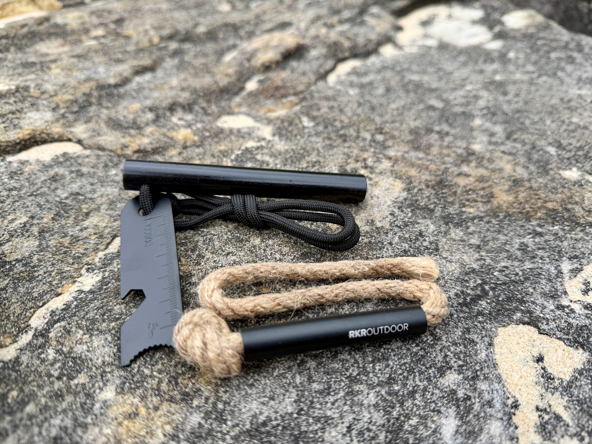 The RKR Outdoor ferro rod, multi-tool striker and tinder wick laid out on a rock