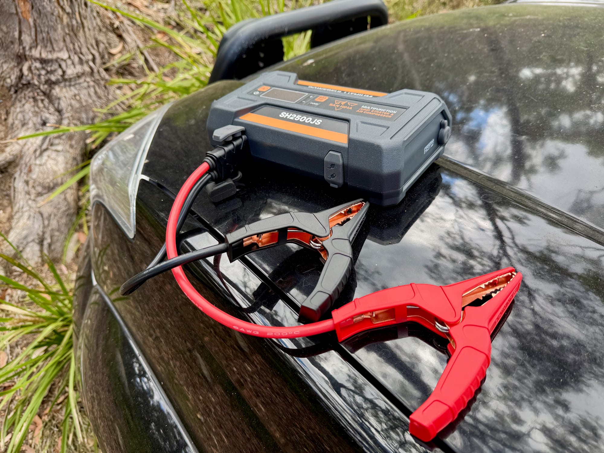 The San Hima jump starter on the bonnet of our car with the red and black clamps connected