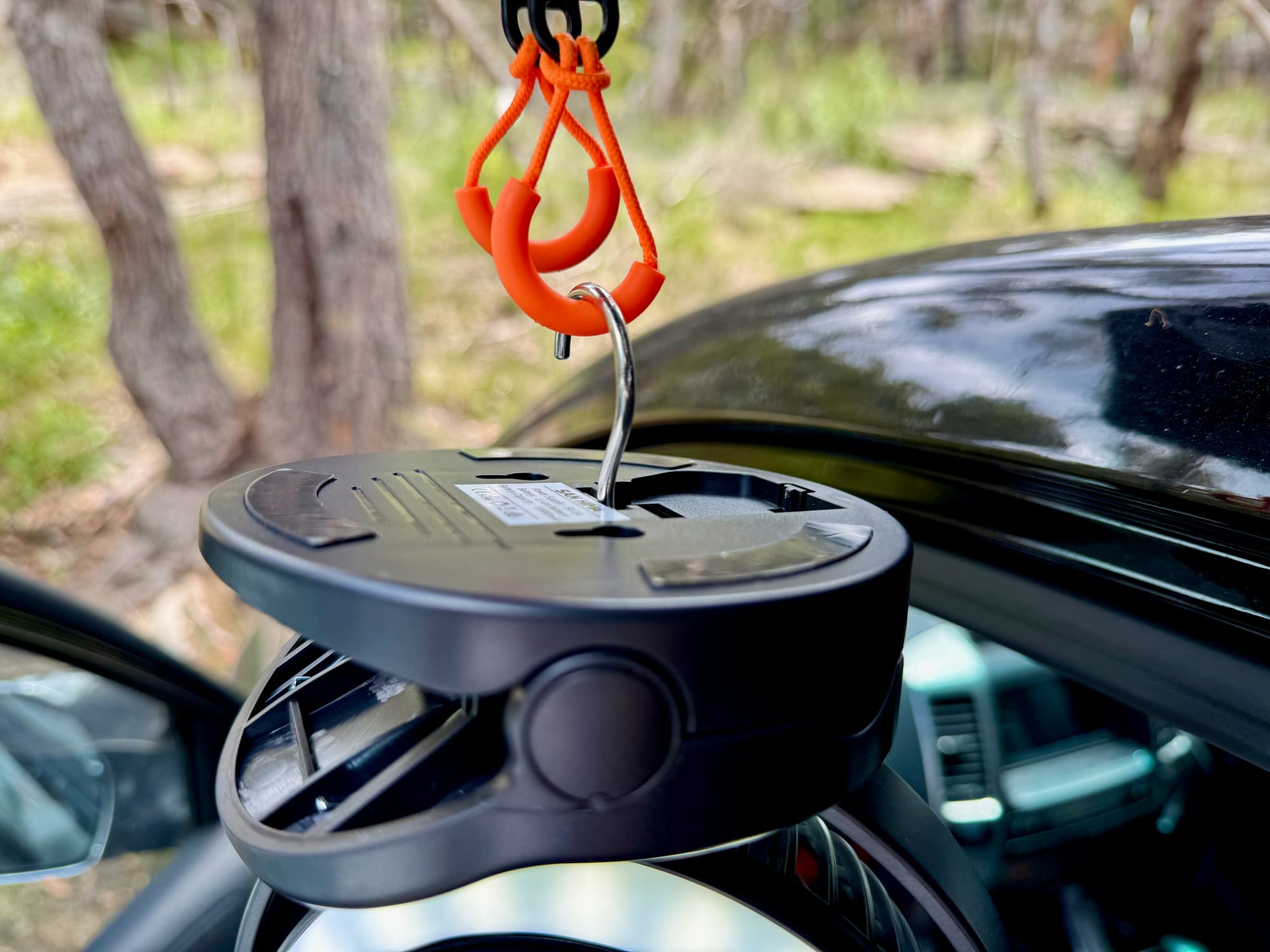 The San Hima clip fan hanging by its fold-out hook from an orange carabiner under a tailgate