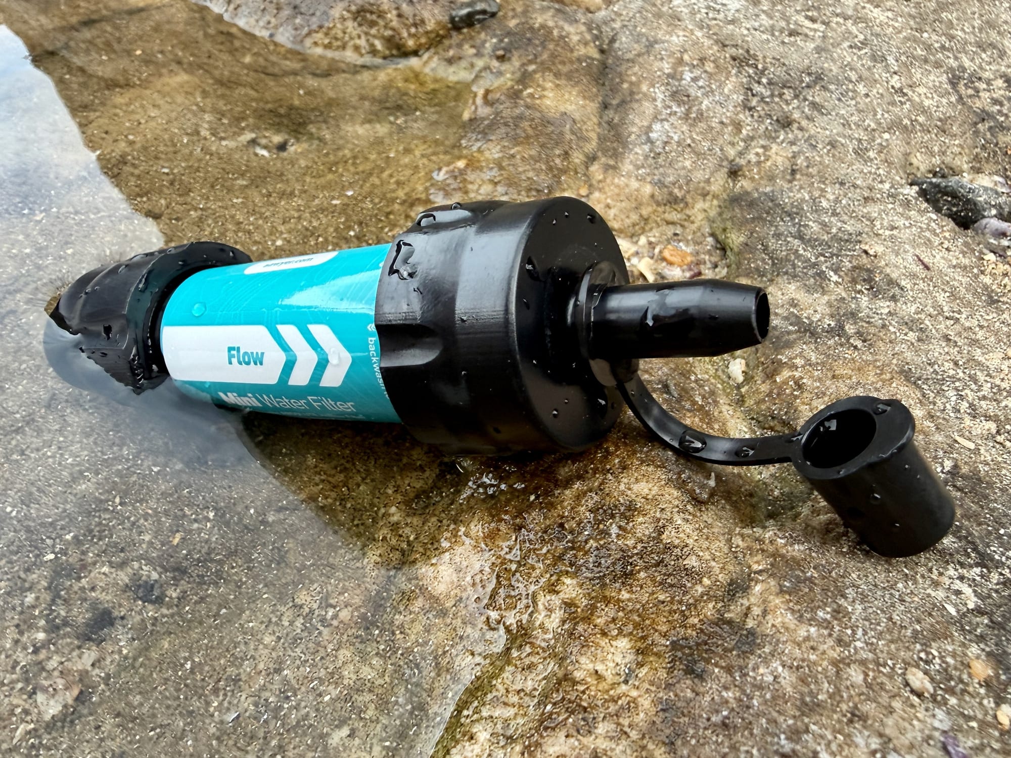 The Sawyer Mini lying in a shallow rock pool with its inlet end in the water and the drinking cap open