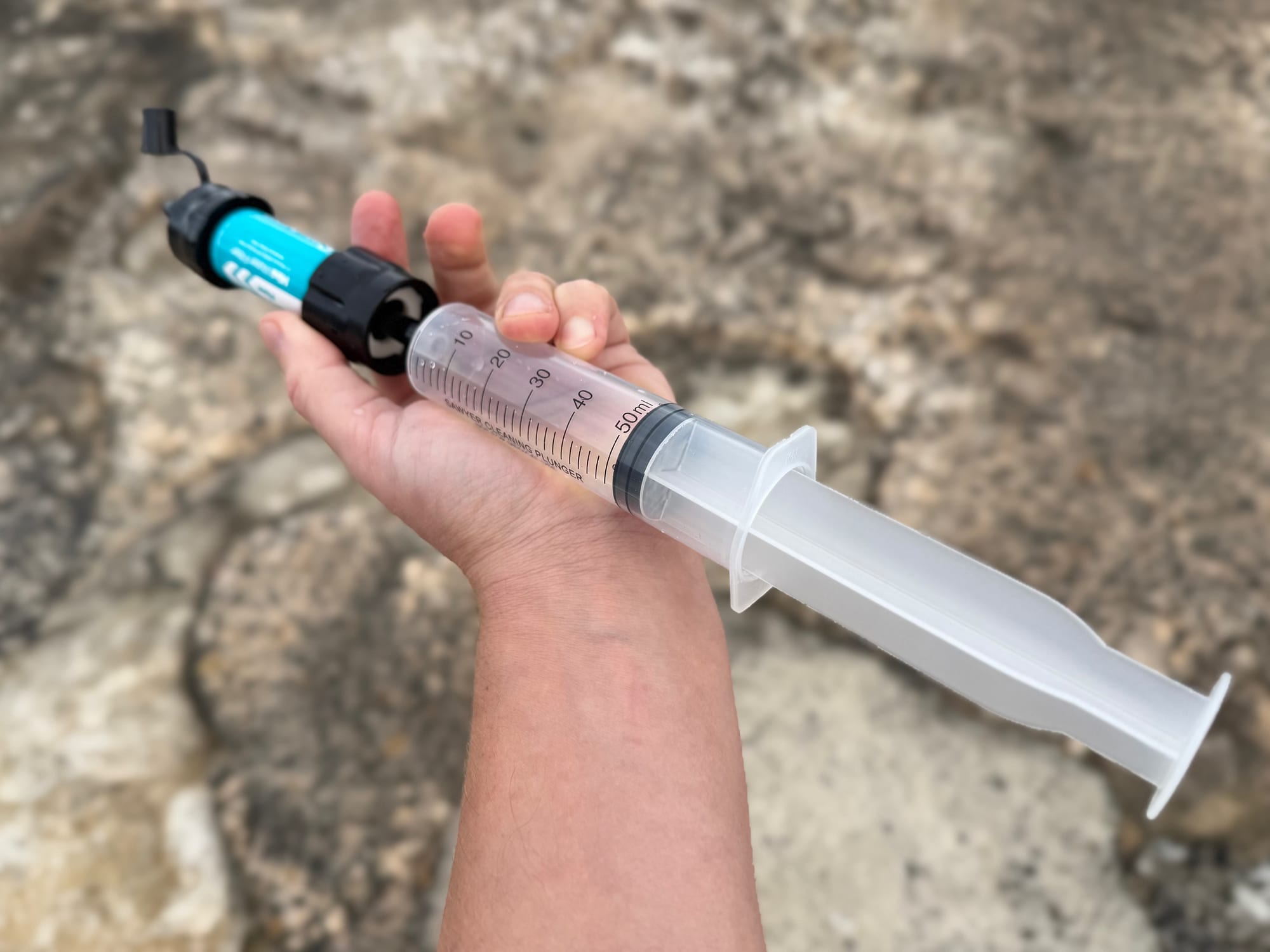 The cleaning plunger pushed onto the Sawyer Mini, held in one hand above a sandstone rock