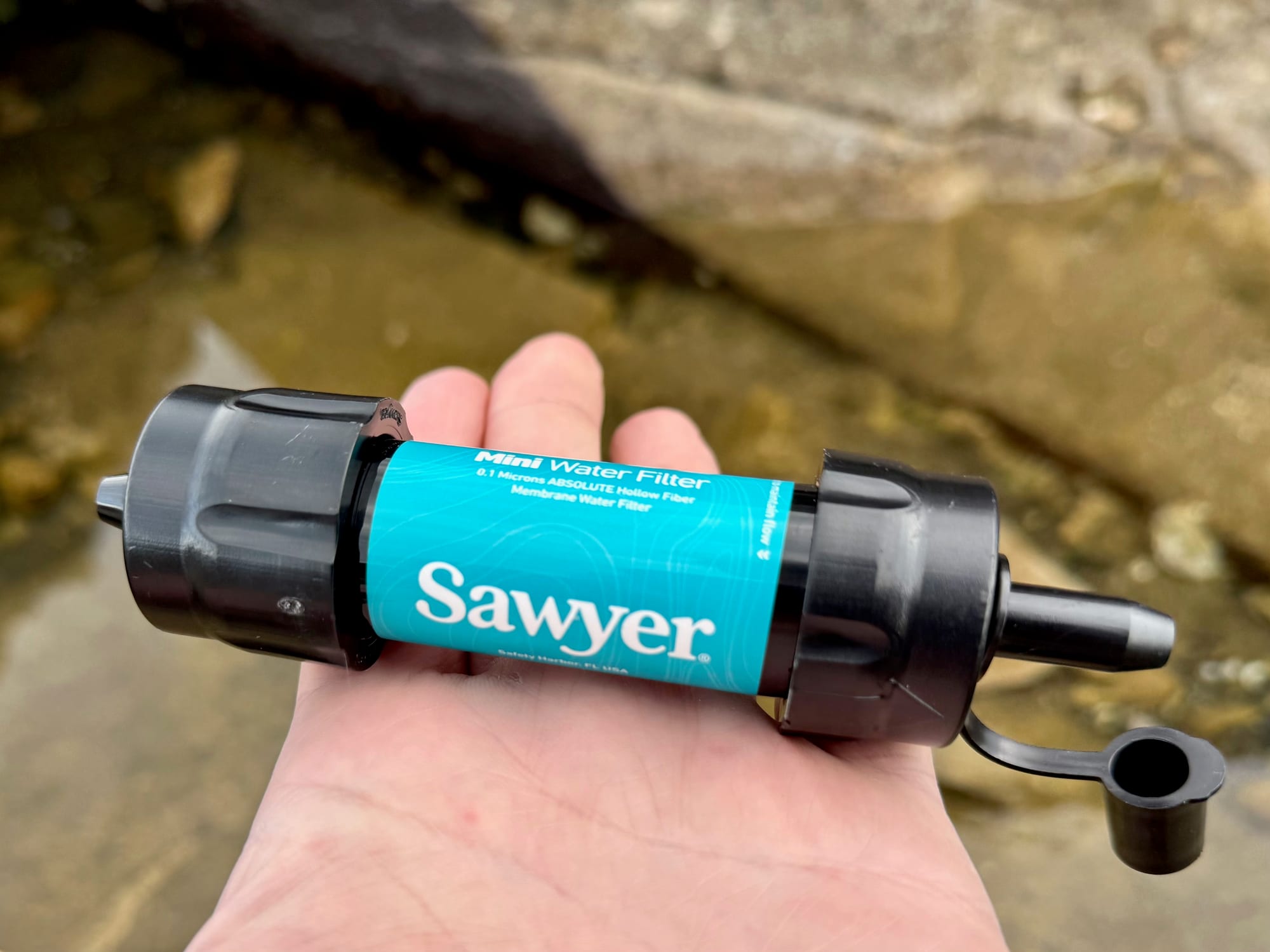 The Sawyer Mini held in the palm of a hand above a rock pool